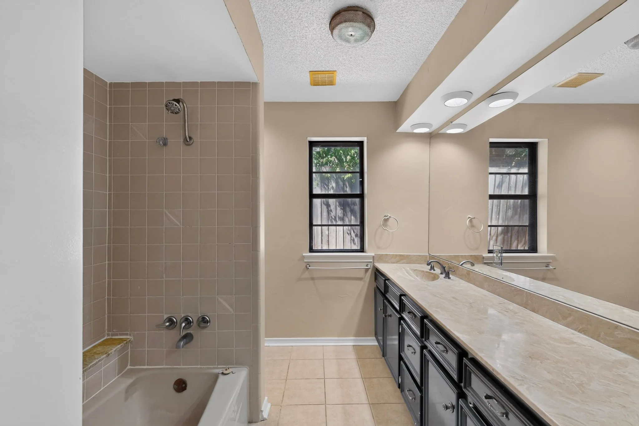 Full-length vanity mirror with overhead lighting, dual windows, and a combination tub-shower with tiled surround and built-in ledge