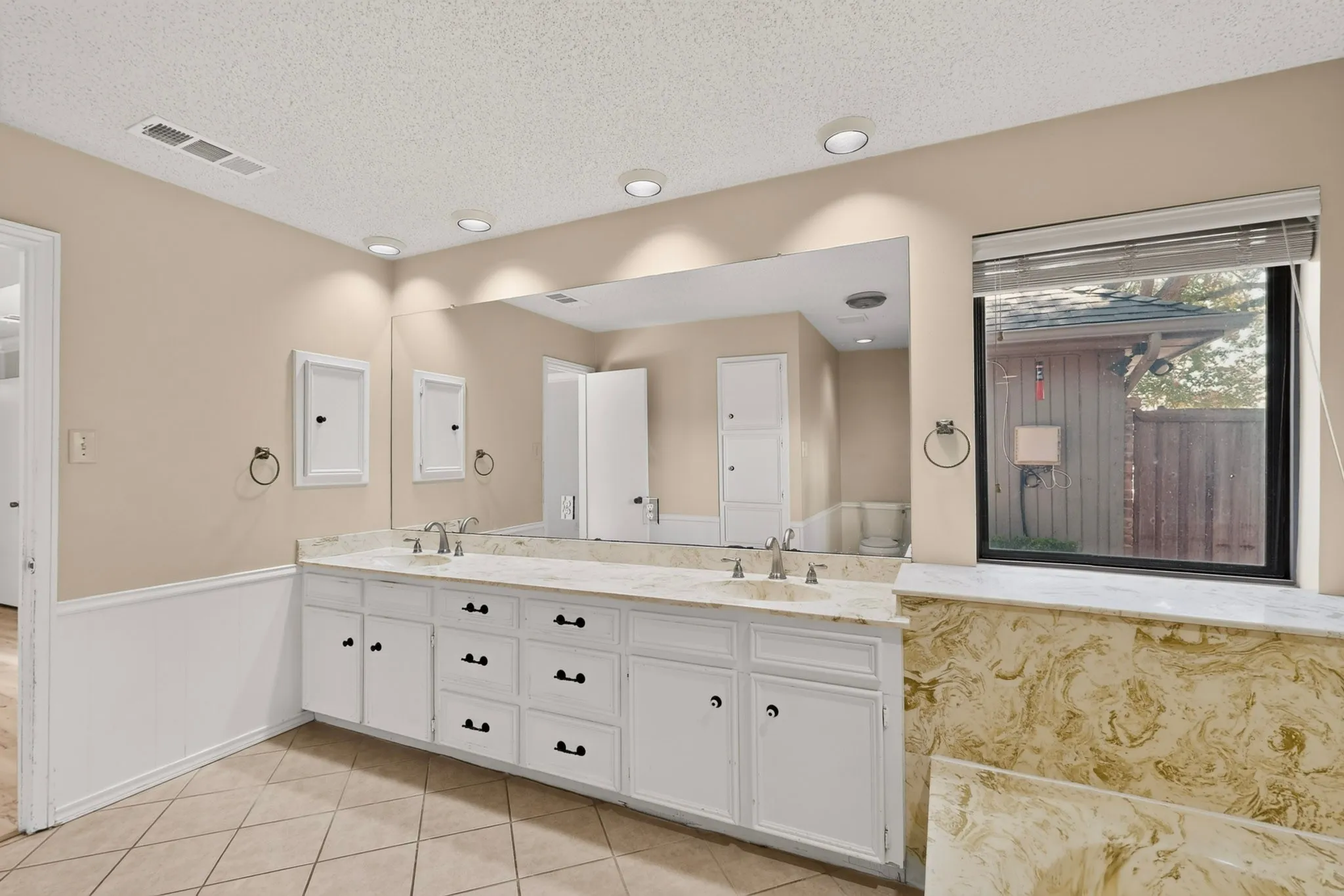 Dual vanity with white cabinetry, integrated sinks, an expansive mirror, and recessed lighting