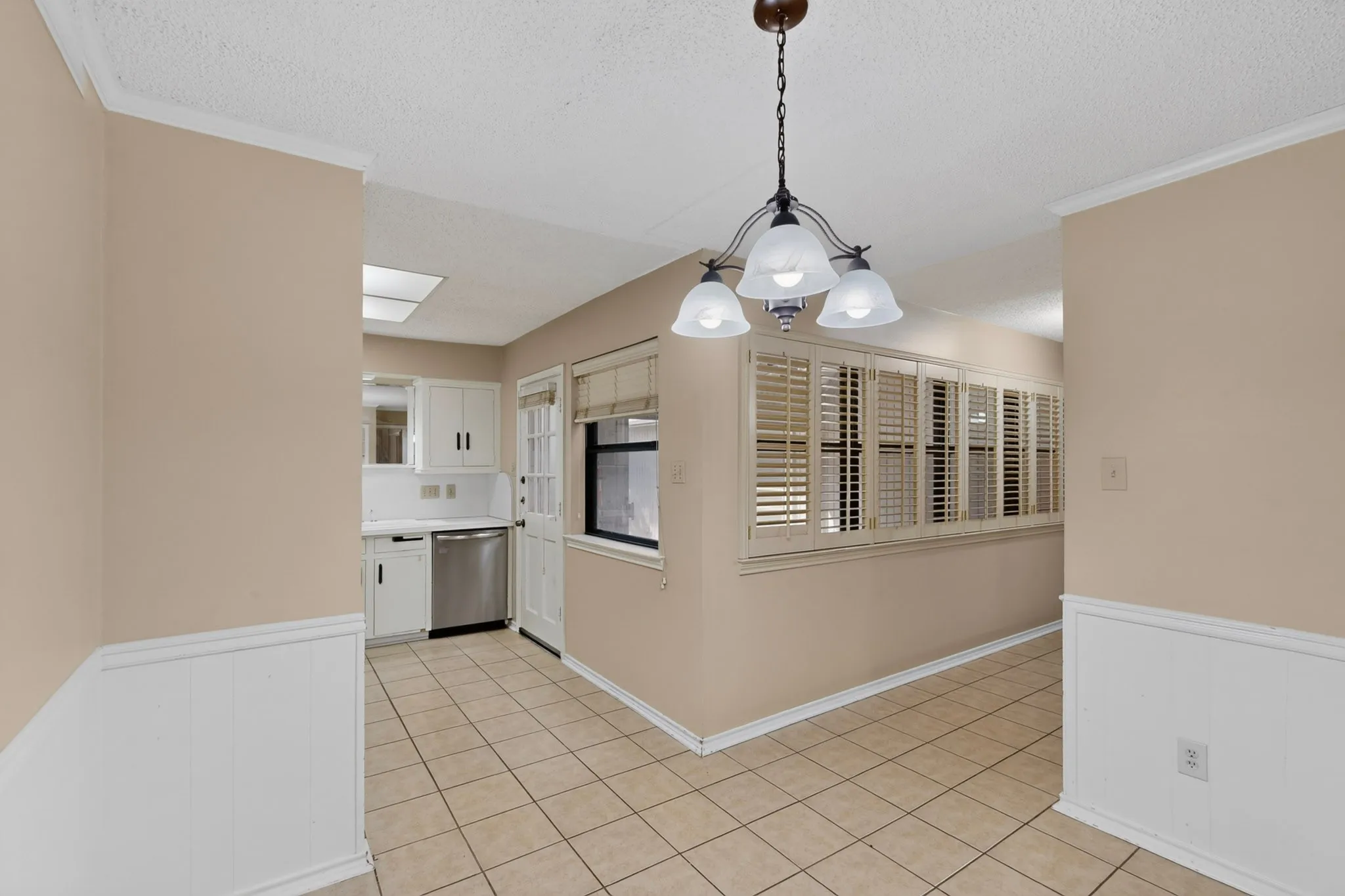 Tiled flooring, wainscoting, wood-finish plantation shutters, ceiling-mounted light fixture, and white cabinetry
