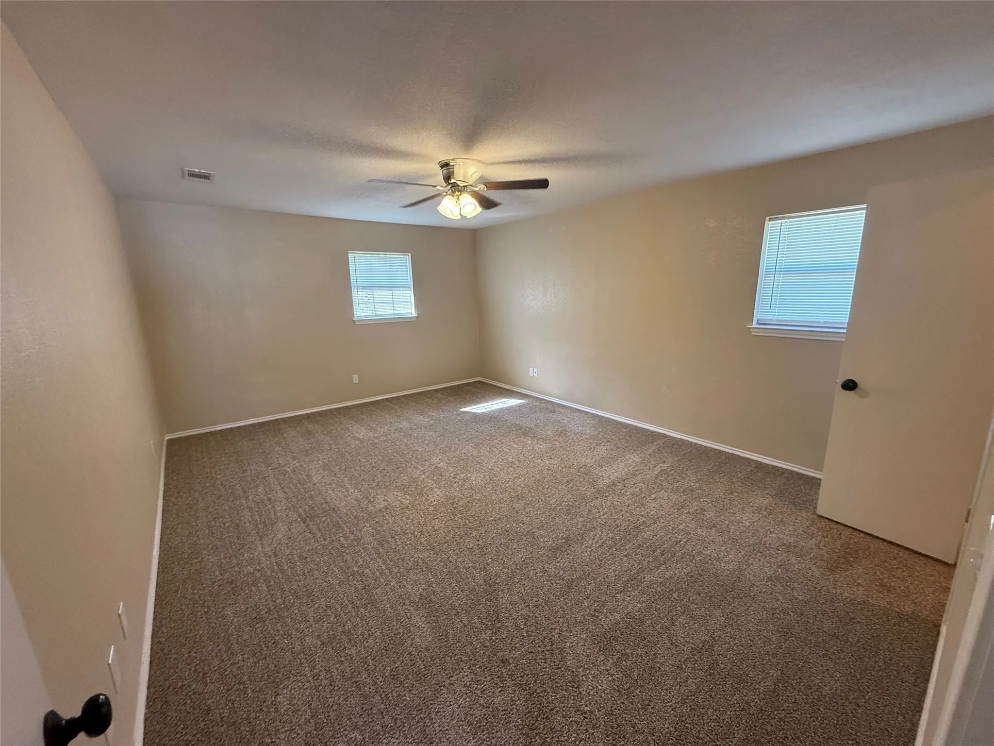 Neutral-toned walls, carpeted flooring, two windows with blinds, and a ceiling fan with integrated lighting