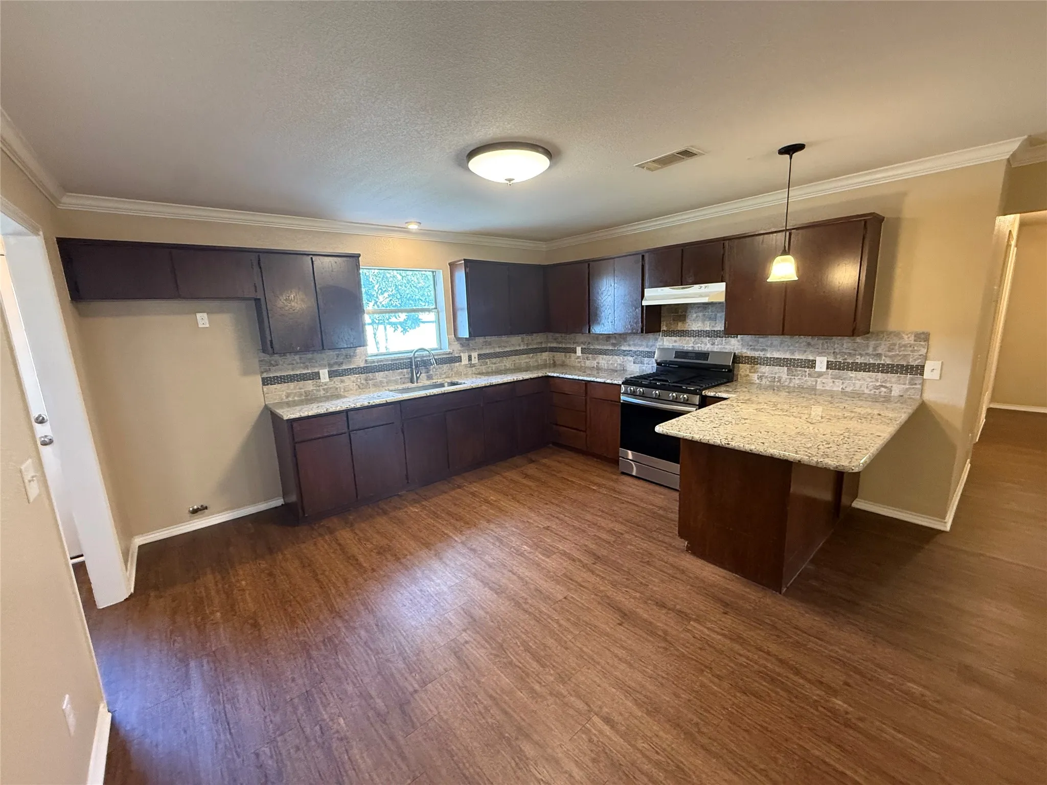 Kitchen featuring wood-finish flooring, dark wood cabinetry, light-toned countertops, tile backsplash, and stainless steel appliances