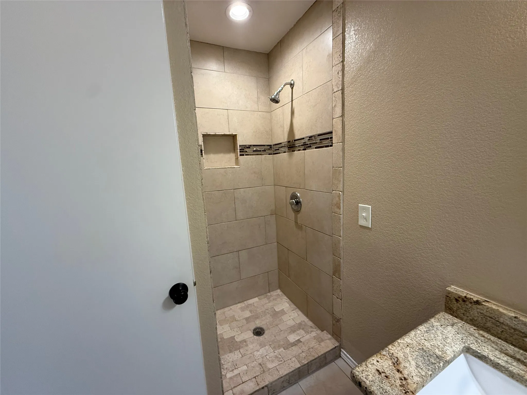 Tiled shower with a decorative mosaic accent band, built-in niche, and overhead recessed lighting