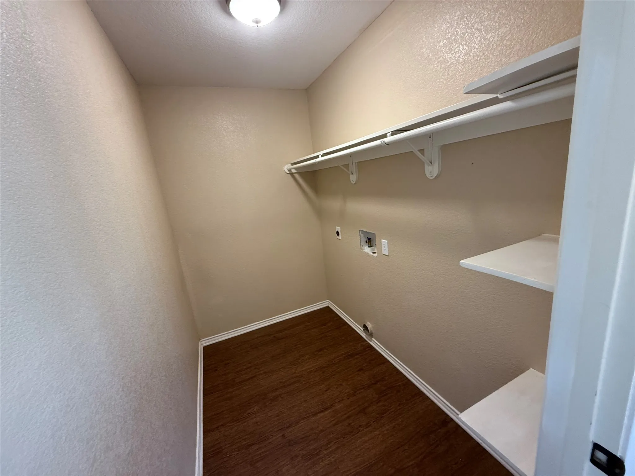 Laundry area featuring wood-finish flooring, overhead lighting, integrated shelving, and a clothing rod