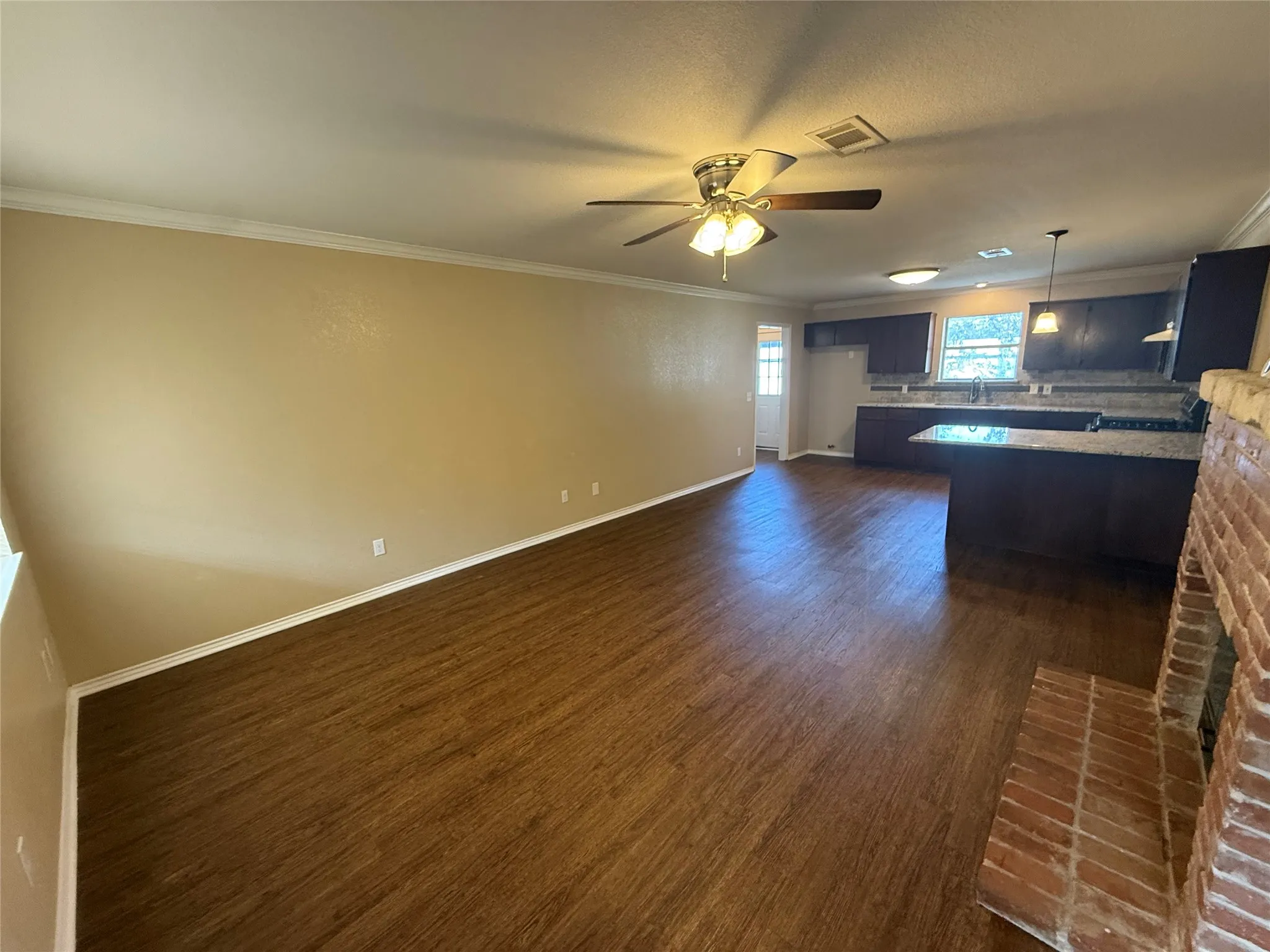 Wood-finish flooring throughout, ceiling fan with integrated lighting, brick fireplace hearth, dark wood cabinetry, and granite countertops