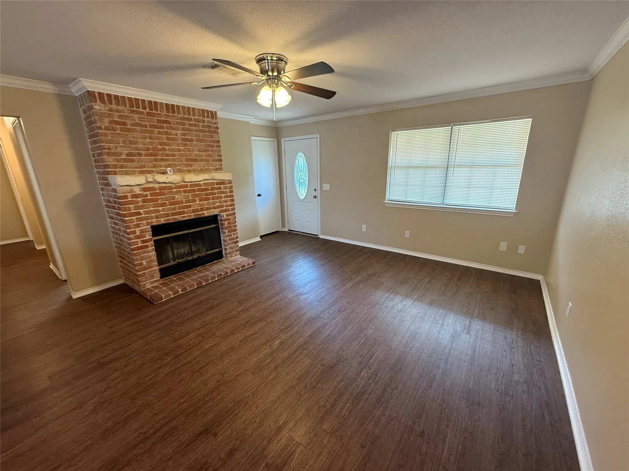 Brick fireplace with a stone mantel, wood-finish flooring, ceiling fan with integrated lighting, and crown molding