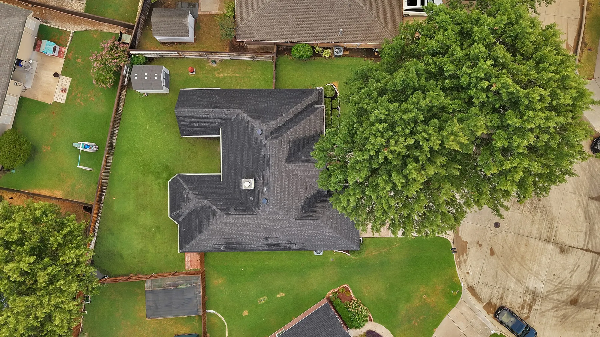 Pitched roof with dark shingles, expansive green lawn, mature trees, and an accessory structure