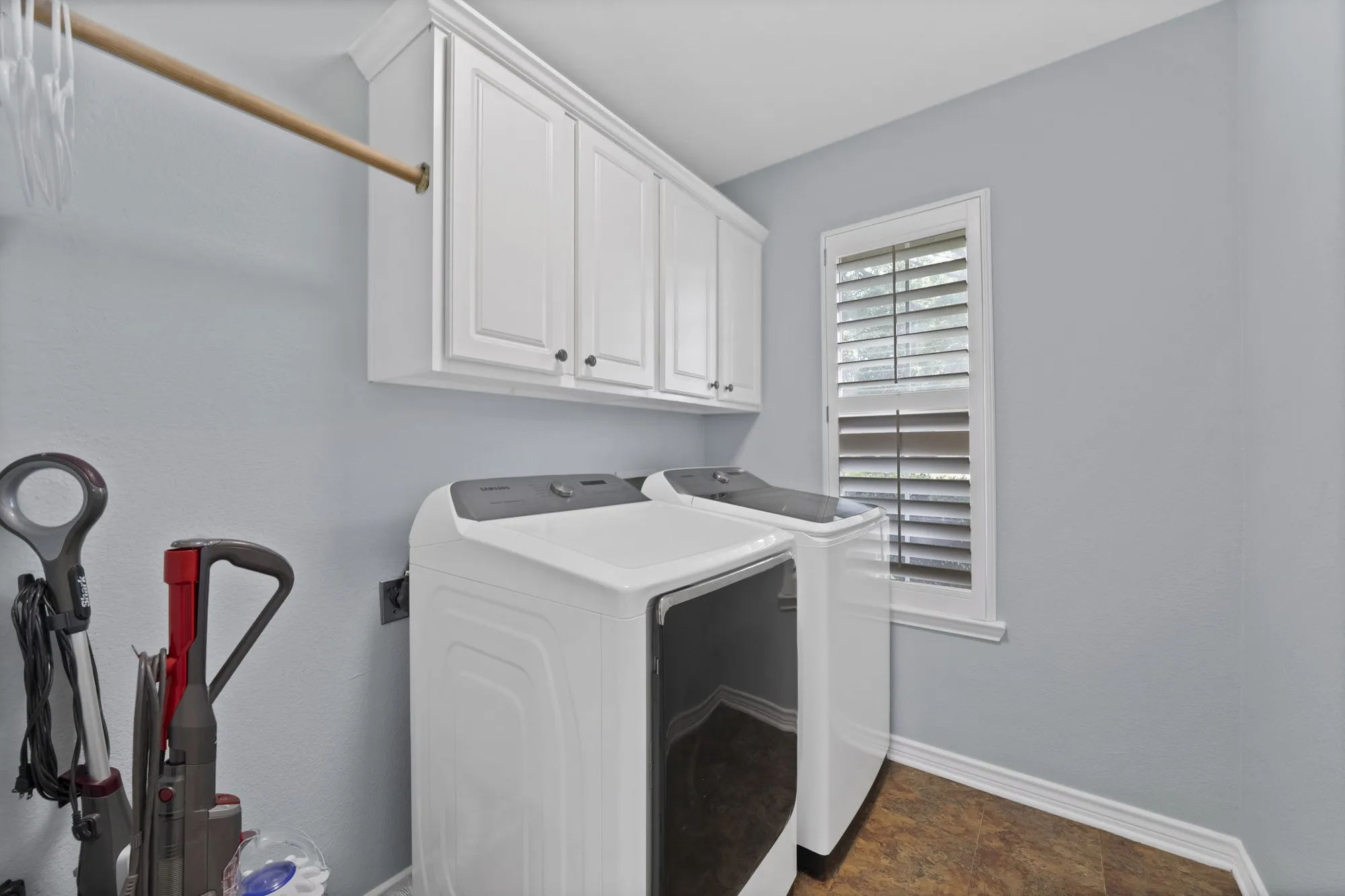 White upper cabinetry, wood-finish flooring, and a window with louvered shutters