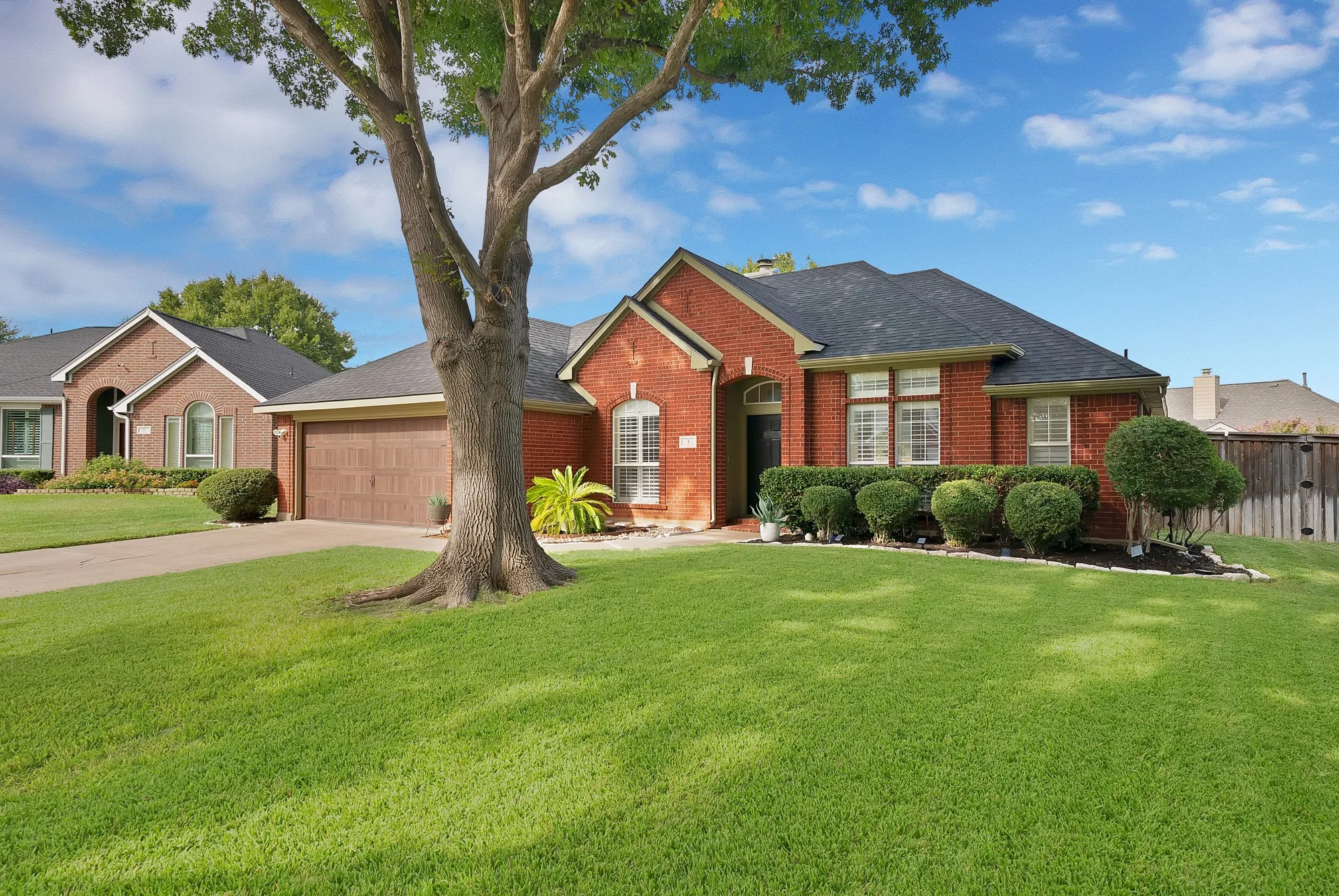 Brick exterior with a dark-pitched roof, featuring a two-car garage with a wood-finish door, arched entry, and established landscaping