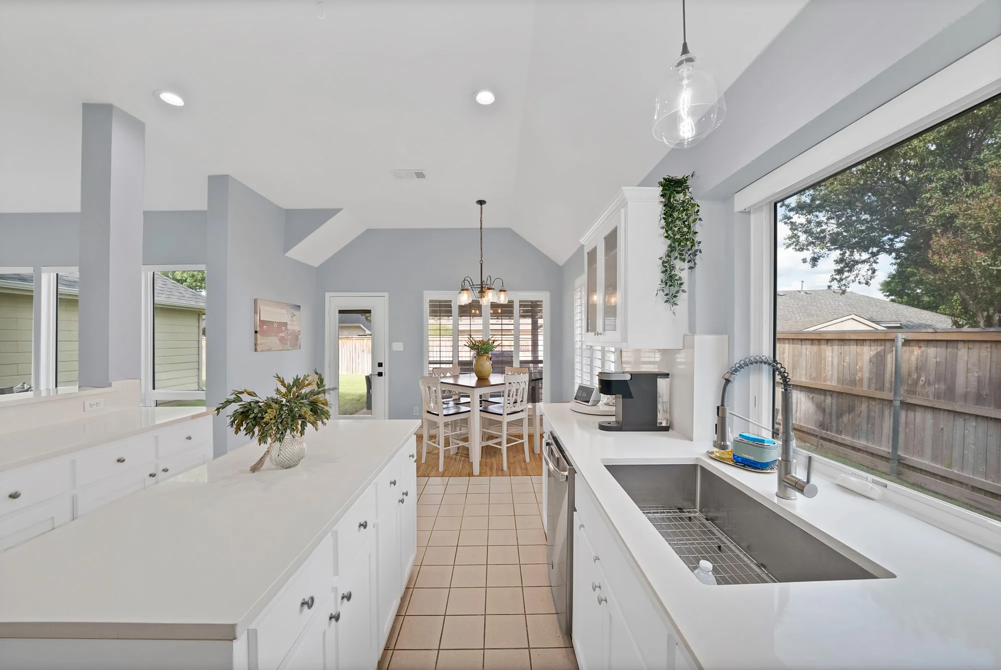 Vaulted ceilings, white cabinetry, a single-basin stainless steel sink, large window, and tile flooring