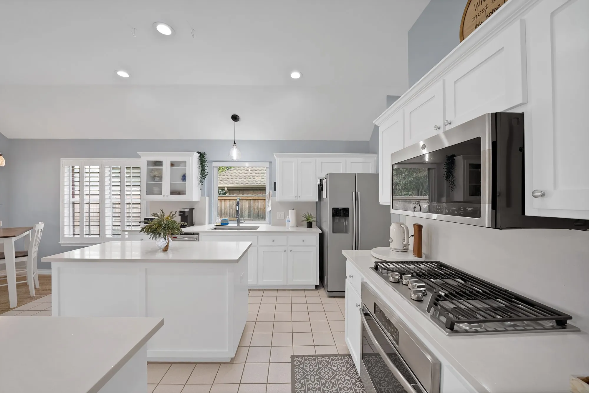 Vaulted ceiling with recessed lighting, white cabinetry, stainless steel appliances, kitchen island, and tile flooring