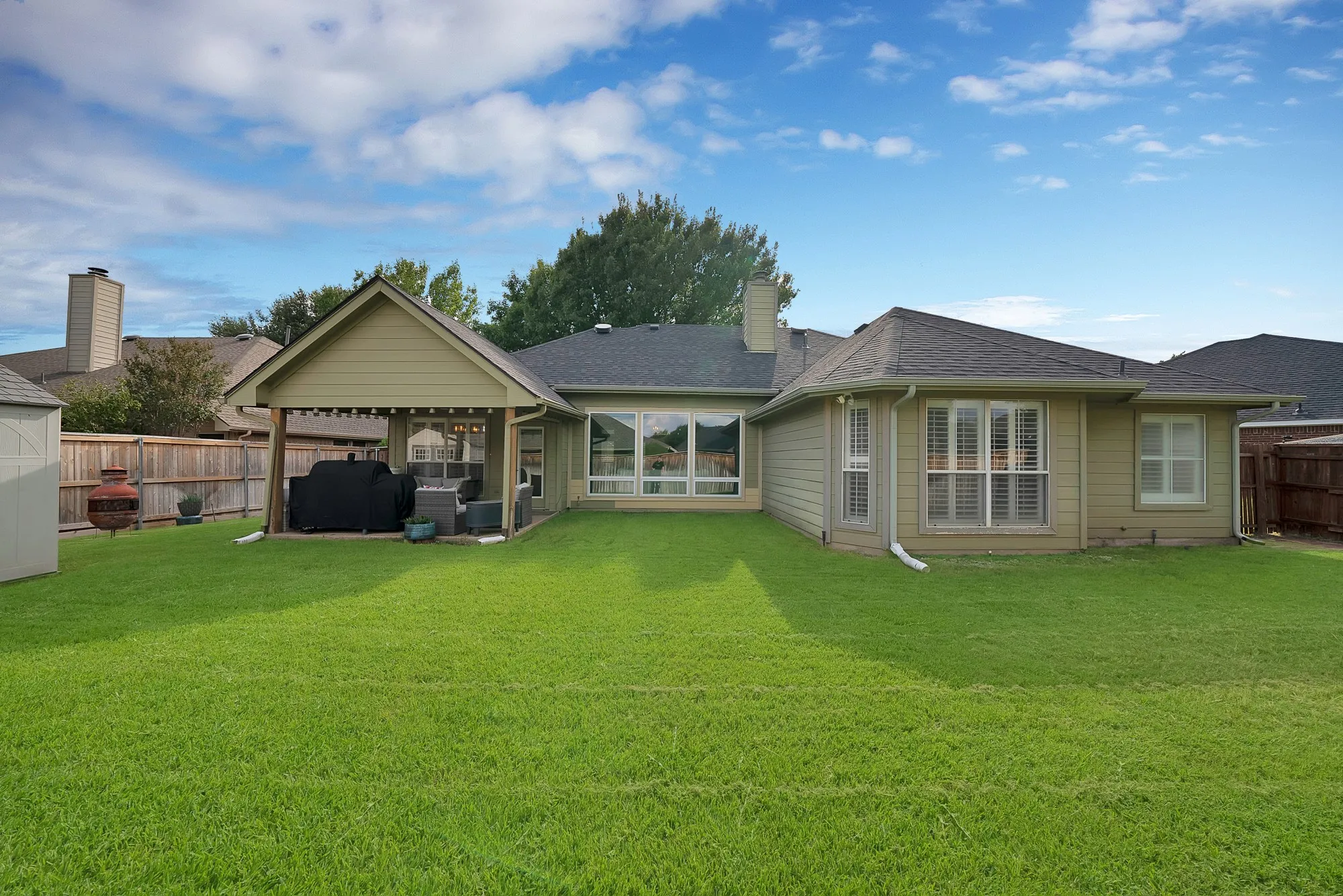 Expansive grass yard with a covered outdoor entertaining area, privacy fencing, and multiple window installations