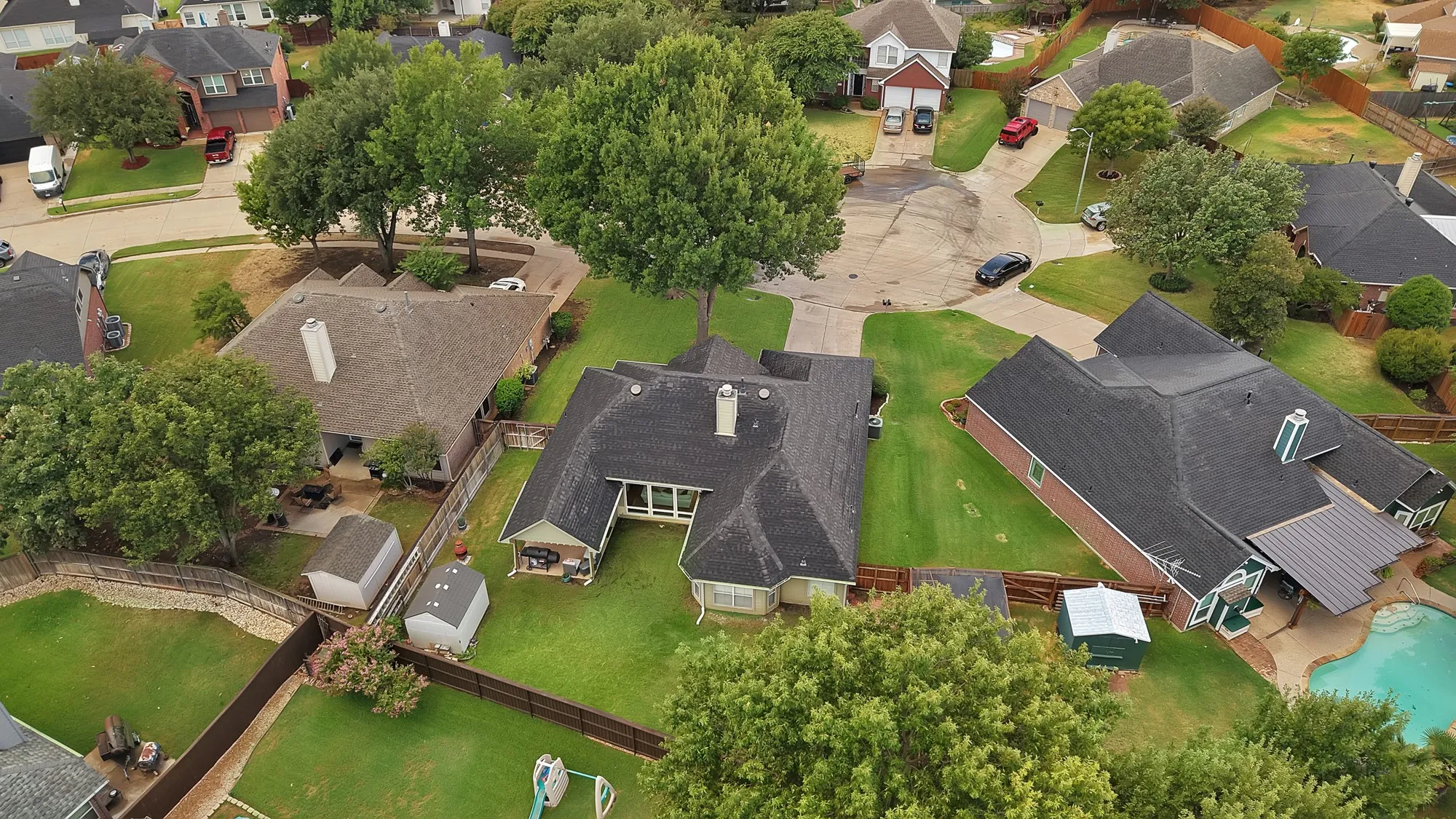 Aerial perspective of a property featuring a swimming pool, a fenced backyard, and multiple storage sheds