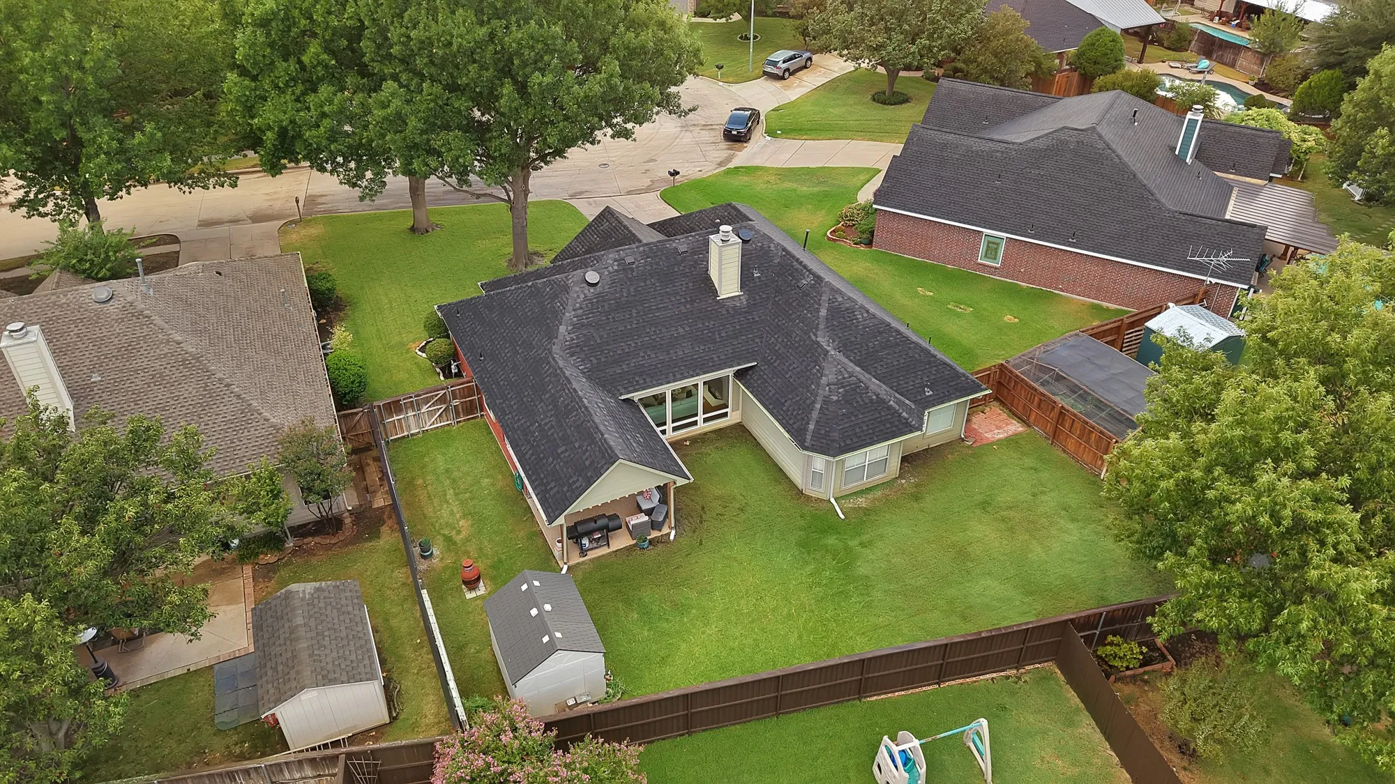 Property featuring a dark shingle roof, expansive green lawn, wood fence, and mature trees
