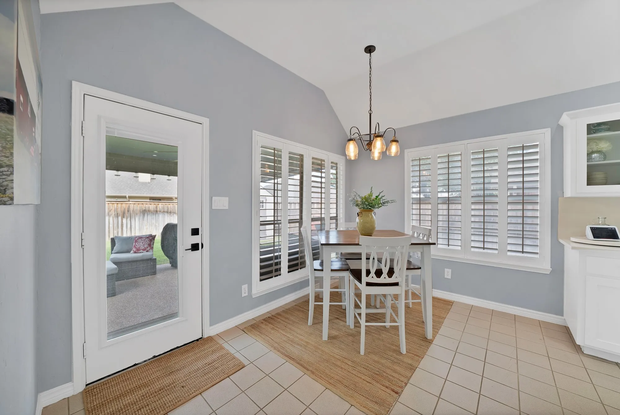 Vaulted ceiling, full-light exterior door, multiple windows with plantation shutters, tile flooring, and a chandelier with amber glass shades