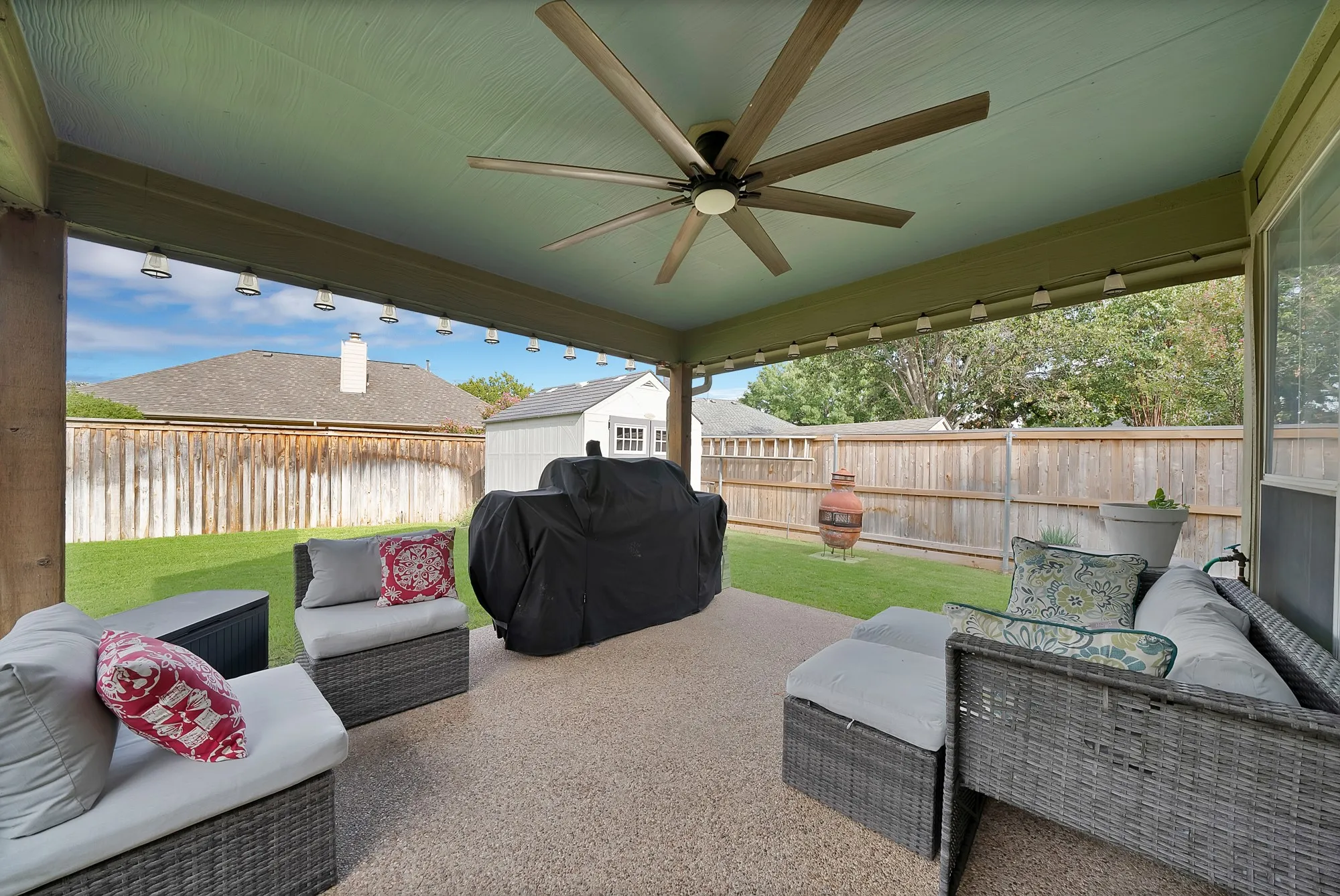 Covered patio with a multi-speed ceiling fan, string lighting, and an aggregate surface
