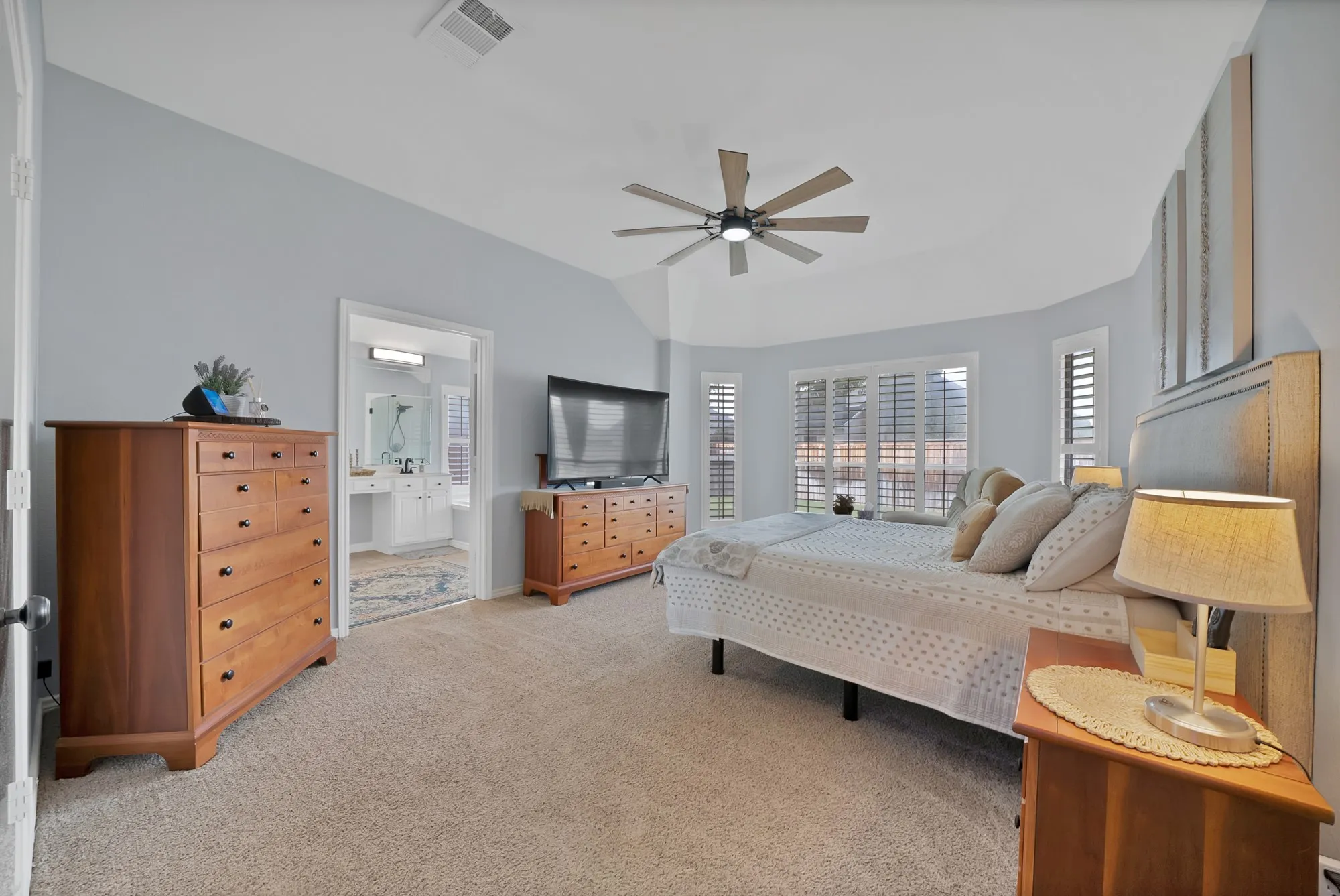 Carpeted flooring with a vaulted ceiling, ceiling fan, and multiple windows featuring plantation shutters
