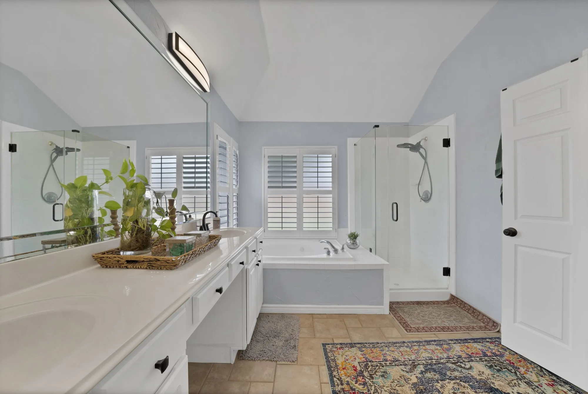 Dual sink vanity with ample counter space, integrated soaking tub, separate glass-enclosed shower, and plantation shutters