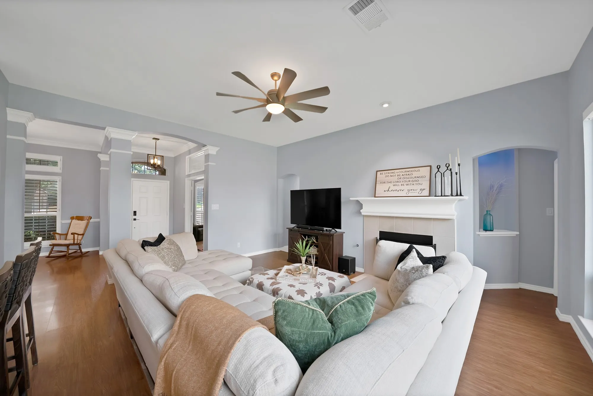 Wood-finish flooring throughout, a ceiling fan with integrated lighting, built-in fireplace with mantel, and an arched wall niche with shelving