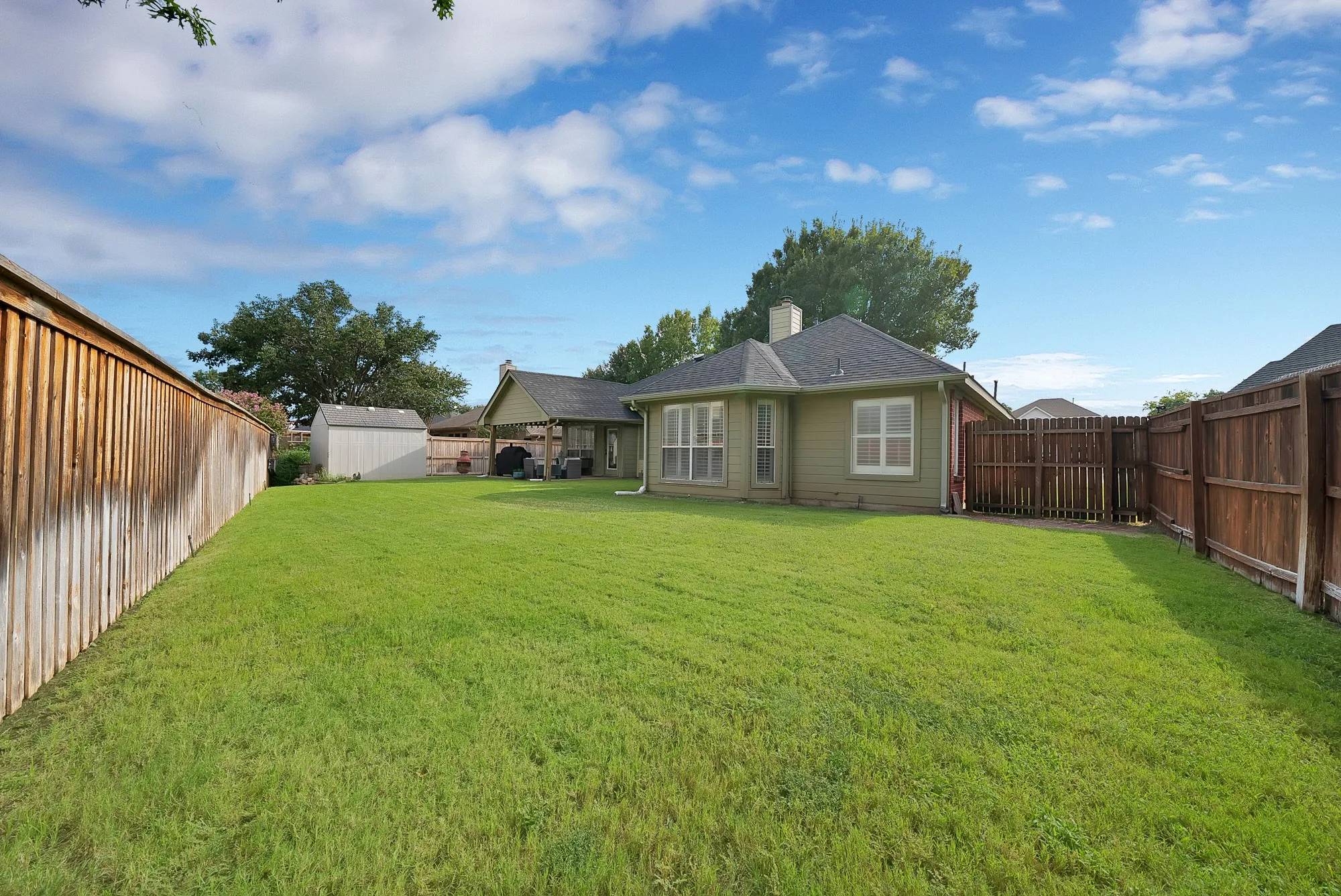 Spacious backyard featuring a manicured lawn, wood privacy fence, and a detached storage shed