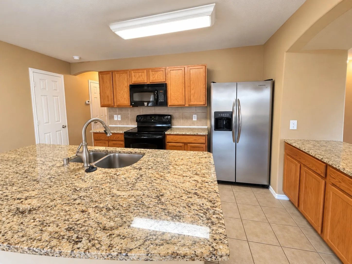 Kitchen featuring an island with a dual basin sink, light wood-finish cabinetry, tile flooring, and stainless steel appliances