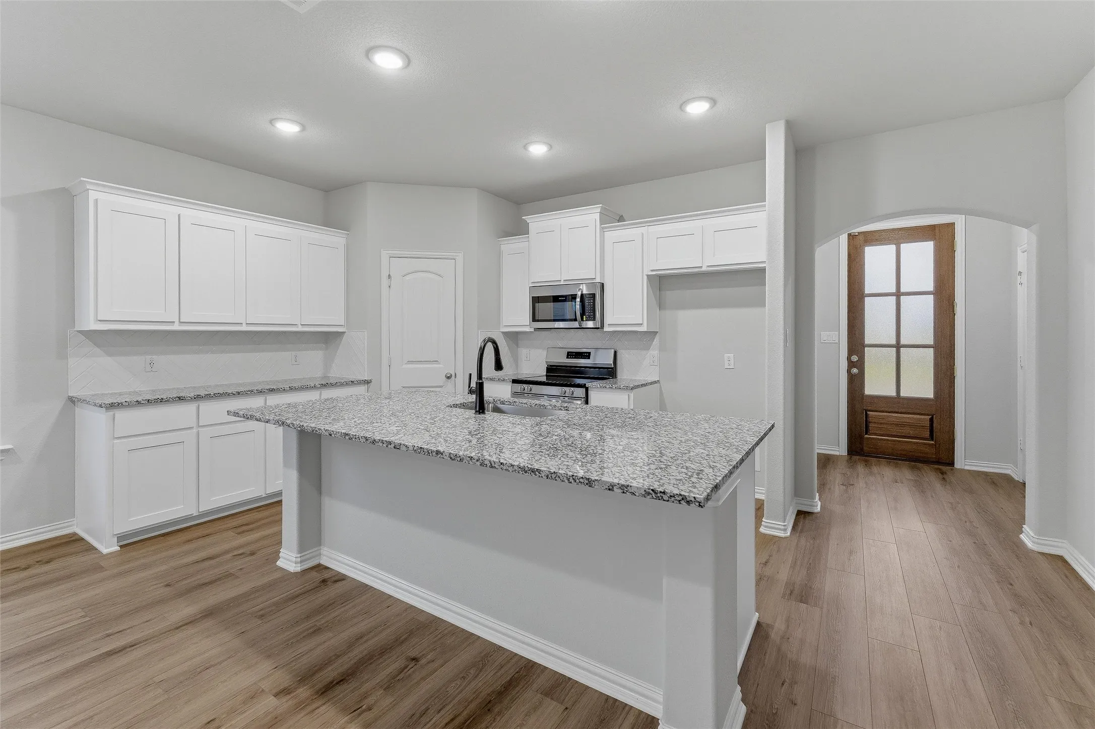 Kitchen featuring a large island with a sink, stainless steel appliances, white cabinetry, granite countertops, and wood-finish flooring