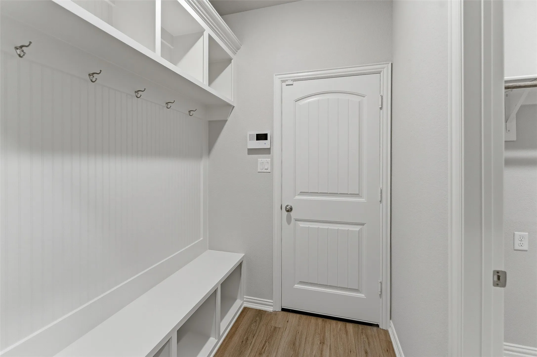 Dedicated mudroom area featuring a built-in bench with storage cubbies, beadboard paneling, coat hooks, upper shelving, and wood-finish flooring