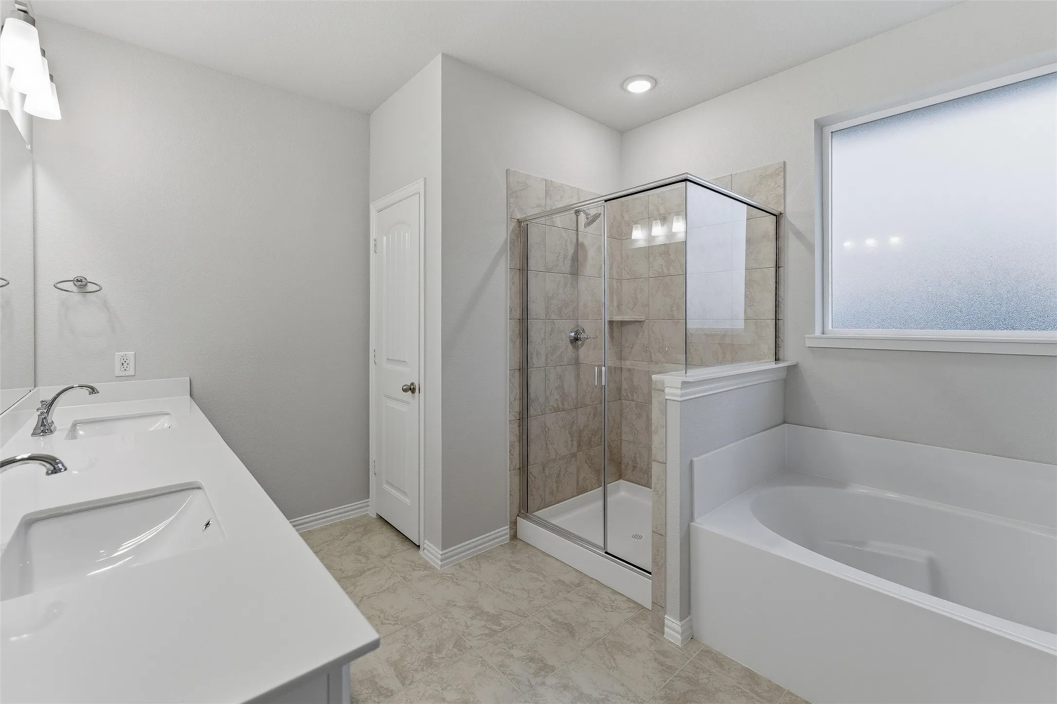 Bathroom featuring a white dual vanity with undermount sinks, a walk-in shower with tile surround and glass enclosure, a built-in bathtub, and a frosted window