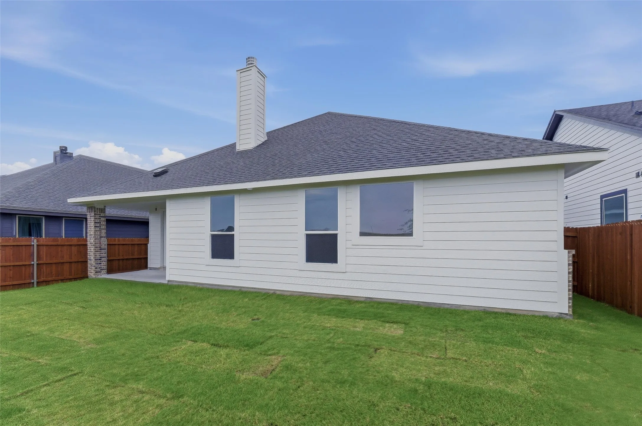 White horizontal siding exterior with a dark shingle roof, featuring a tall chimney and multiple windows