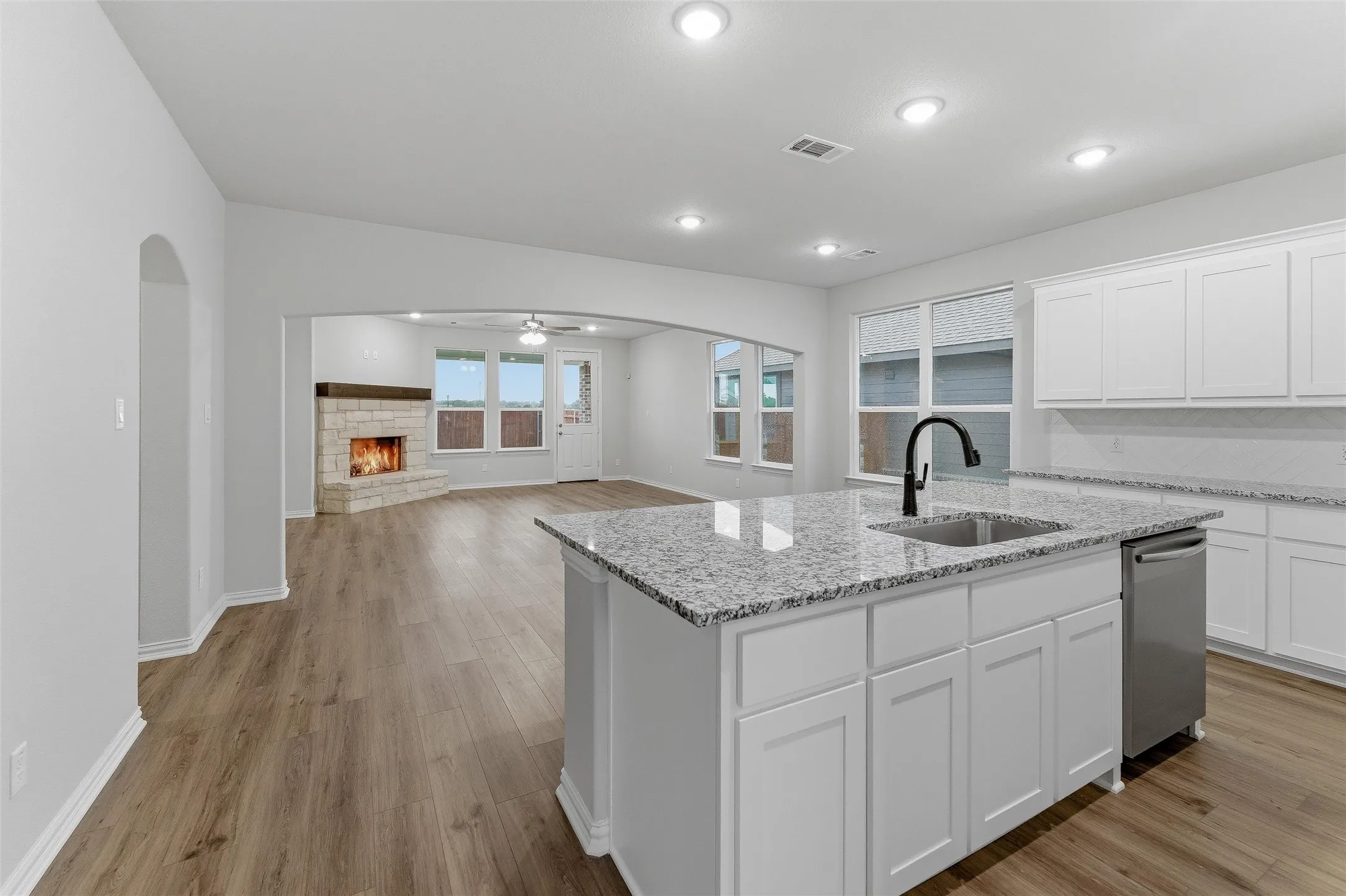 Kitchen island featuring a stainless steel sink with a matte black faucet, granite countertops, white cabinetry, and wood-finish flooring