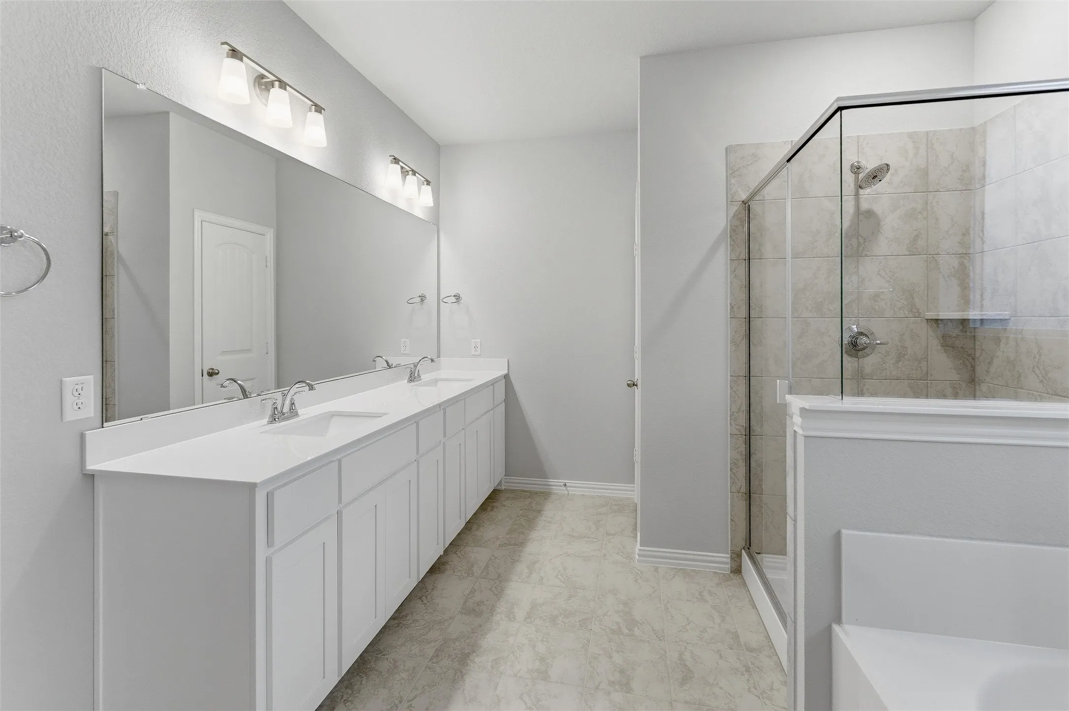 Spacious bathroom featuring a dual vanity with white cabinetry and countertops, a large frameless mirror, and overhead vanity lighting