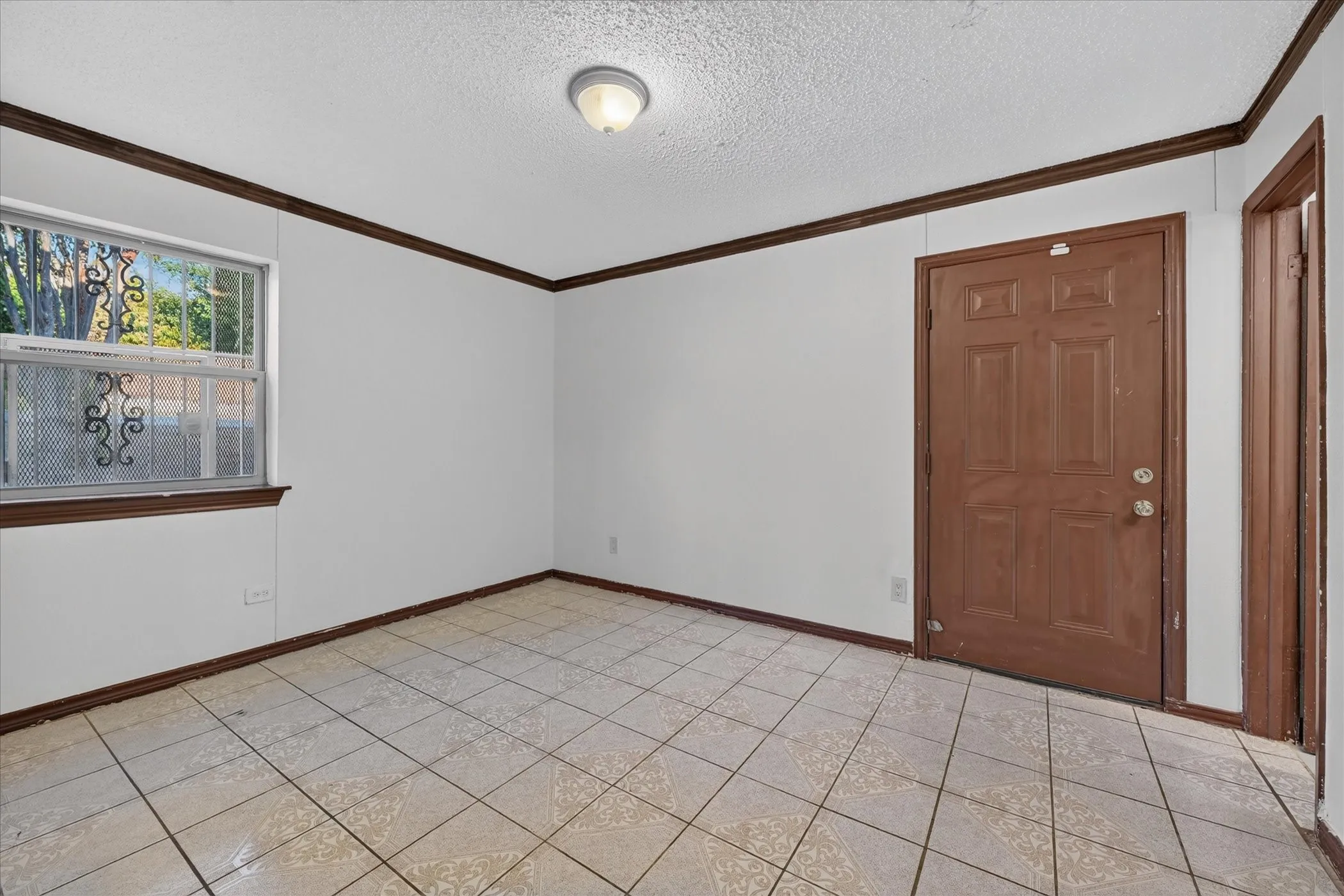 Recessed ceiling light fixture, white walls, wood-finish trim, tile flooring, and a single window with security bars