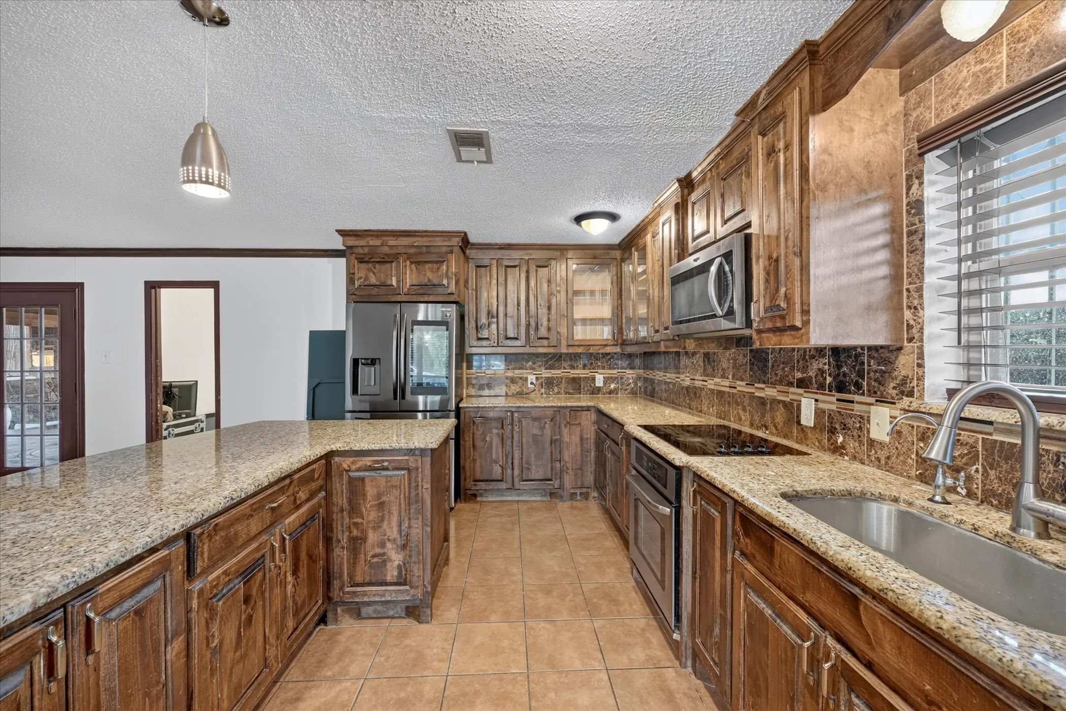 Kitchen featuring granite-style countertops, wood-finish cabinetry, stainless steel appliances, a tile backsplash, and ceramic tile flooring
