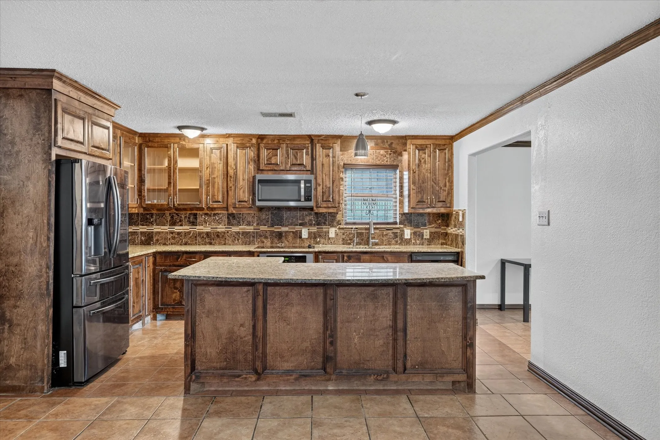 Kitchen featuring wood cabinetry, stainless steel appliances, a center island with a granite-style countertop, and tile flooring