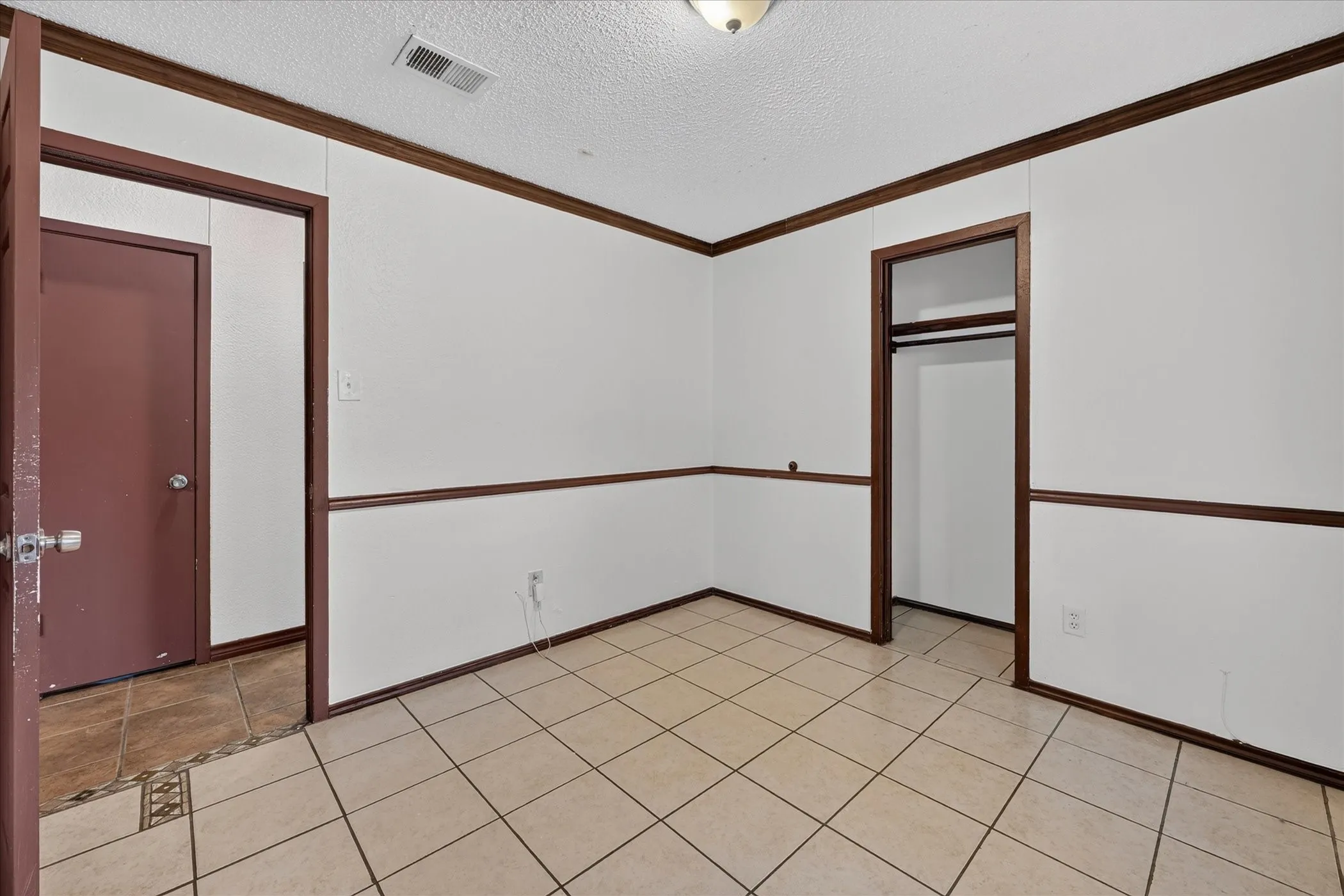Tile flooring with a matte finish, white wall panels with dark trim, and a built-in closet with hanging rod