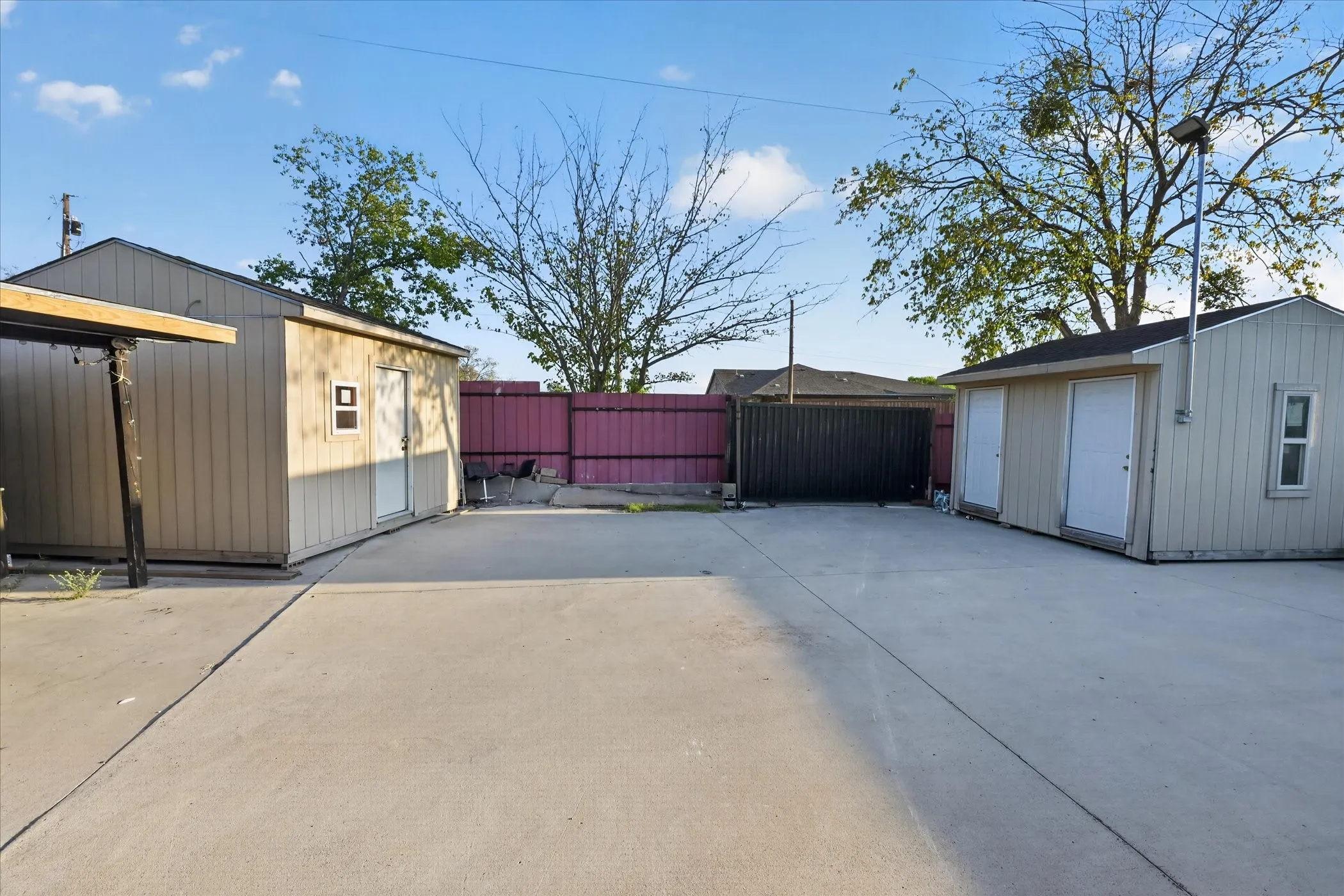 Expansive concrete pad with two detached utility structures, a partial covered awning, and a privacy fence