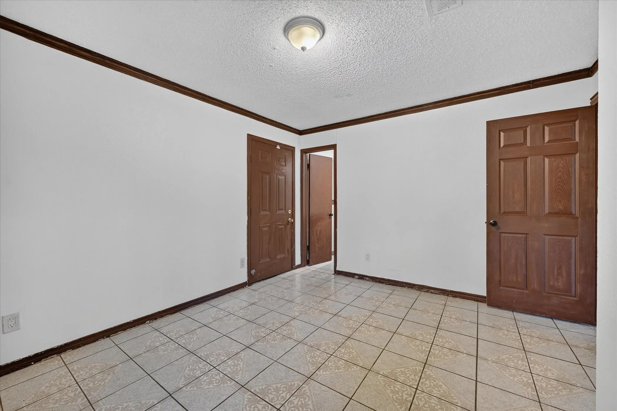 White walls with dark wood-finish trim, a flush-mount ceiling light, and light-colored tile flooring