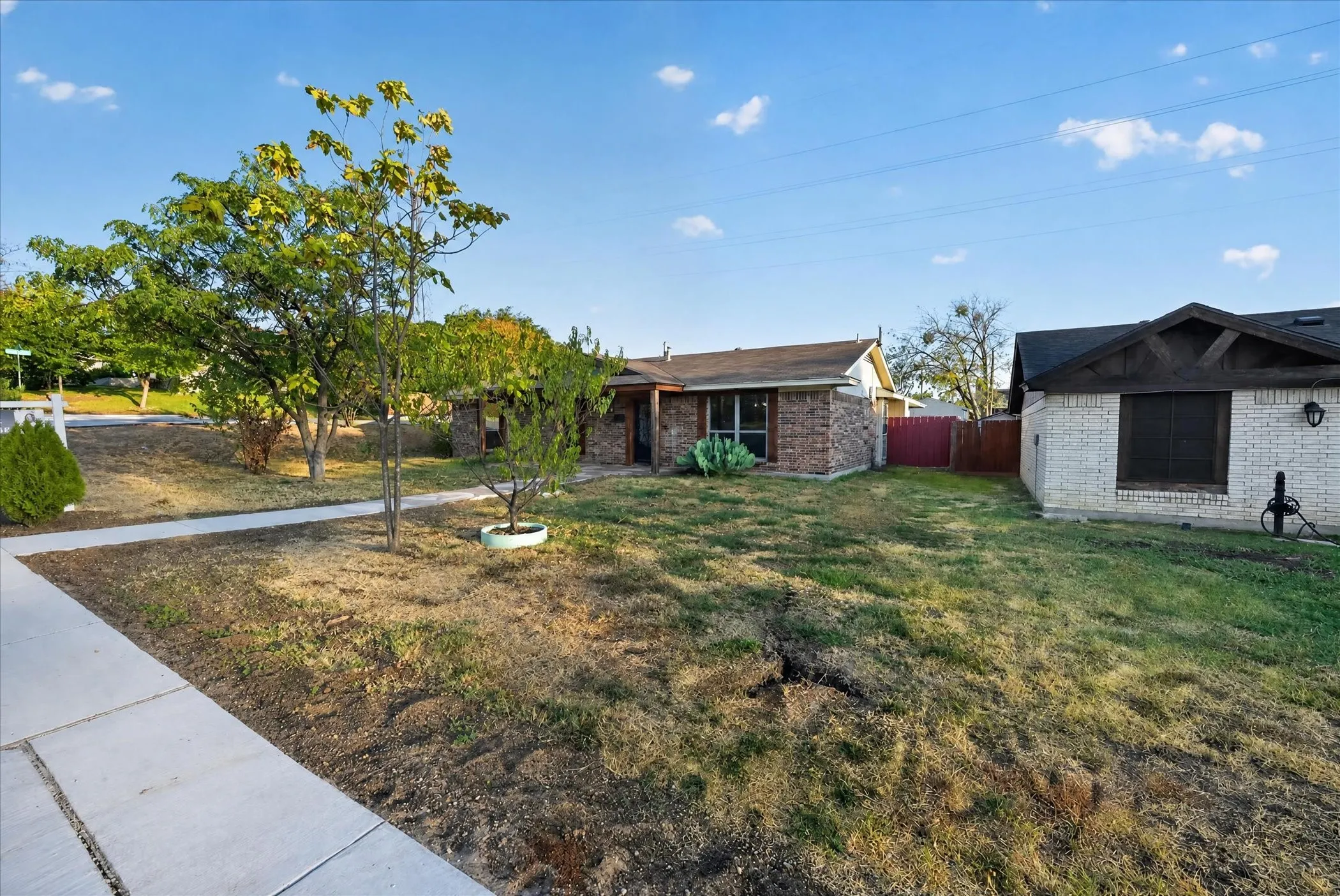 Brick exterior, mature trees, concrete walkway, sloped lot, partial fencing