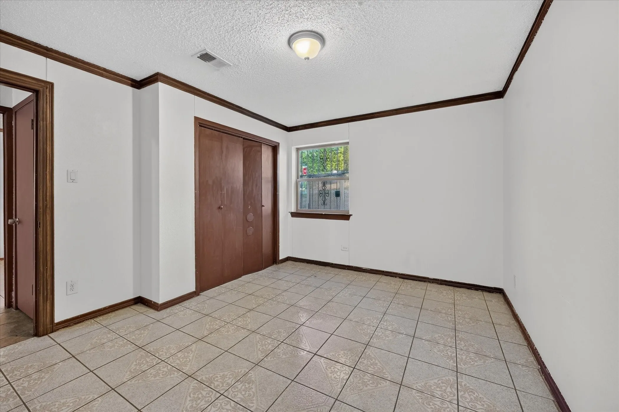 Tile flooring, white walls, wood trim, flush mount ceiling light, and a window with security bars