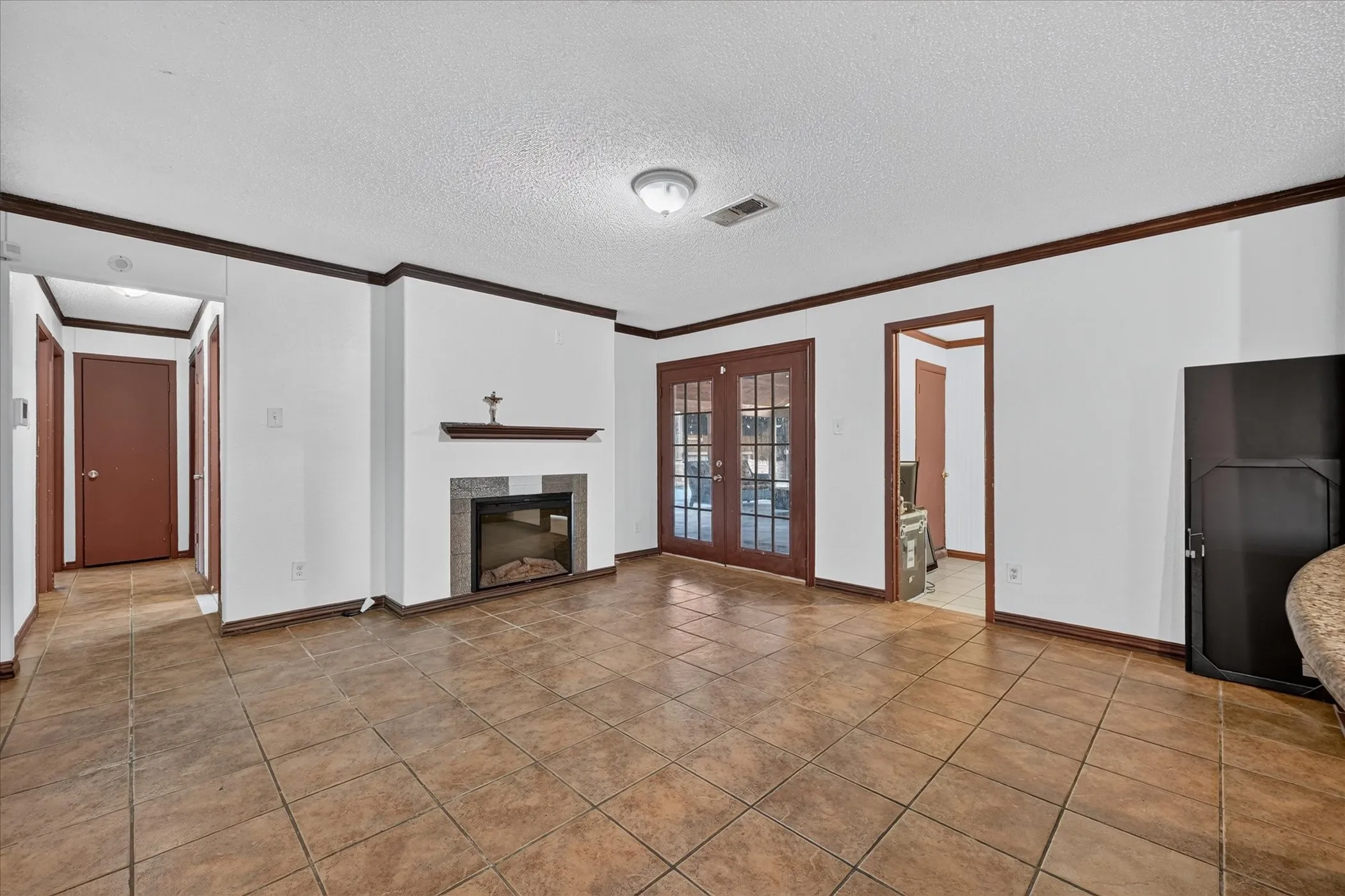 Tile flooring, a fireplace with a stone surround, wood trim accents, and French doors