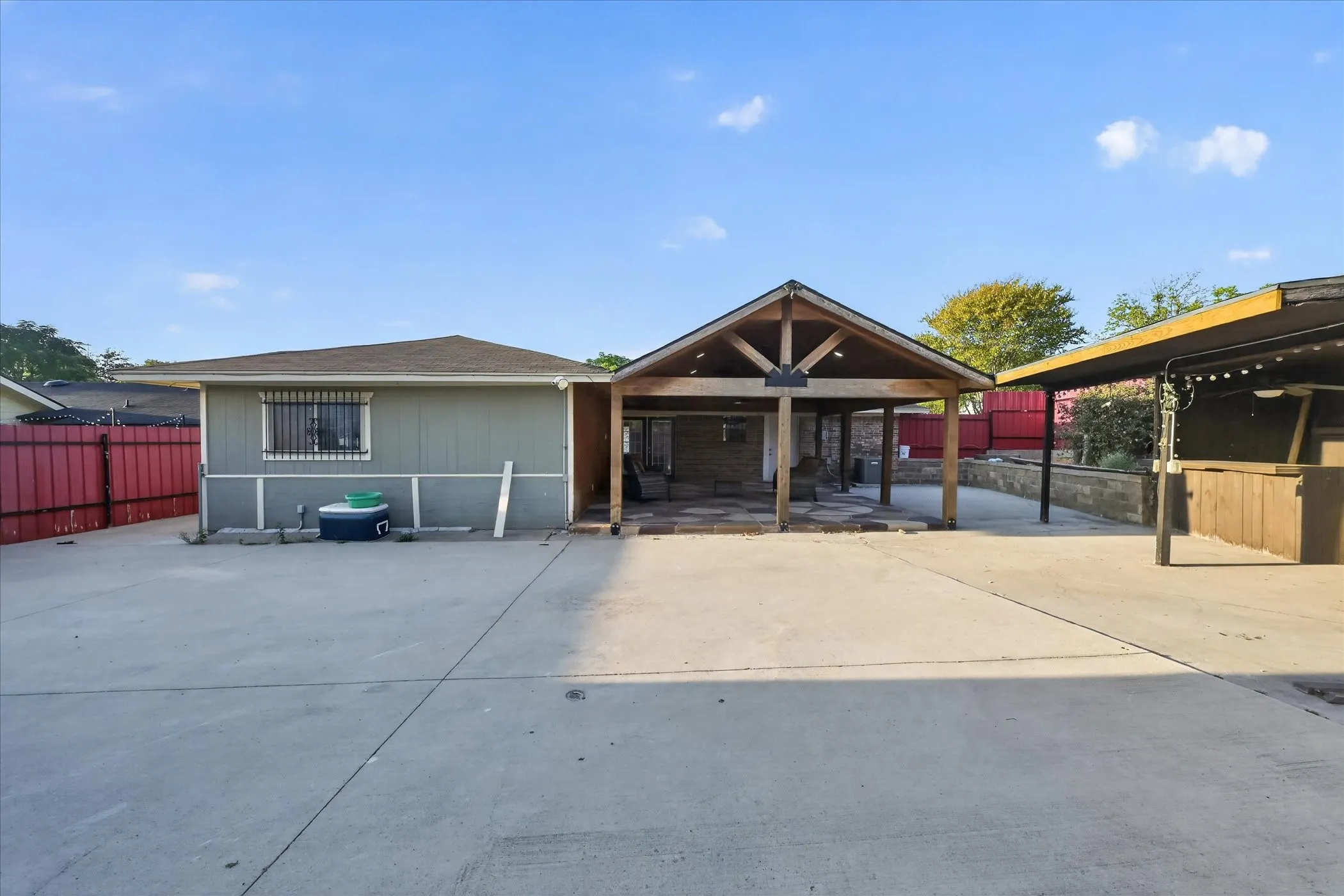 Expansive concrete patio area with a covered outdoor structure featuring exposed wood beams, a gabled roof, and a built-in bar area with a flat roof