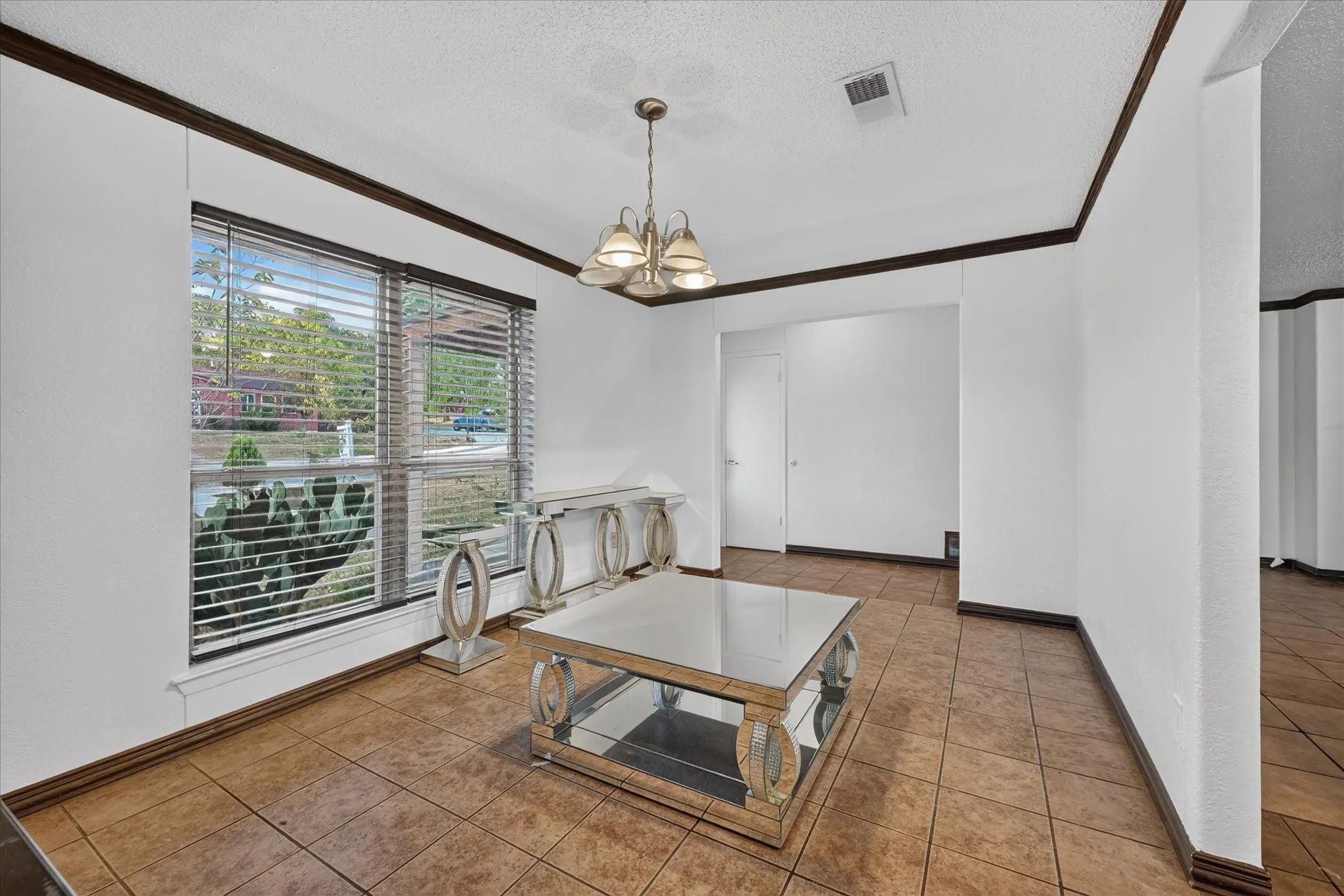 Spacious room featuring tile flooring, a large window with blinds, and a multi-light chandelier