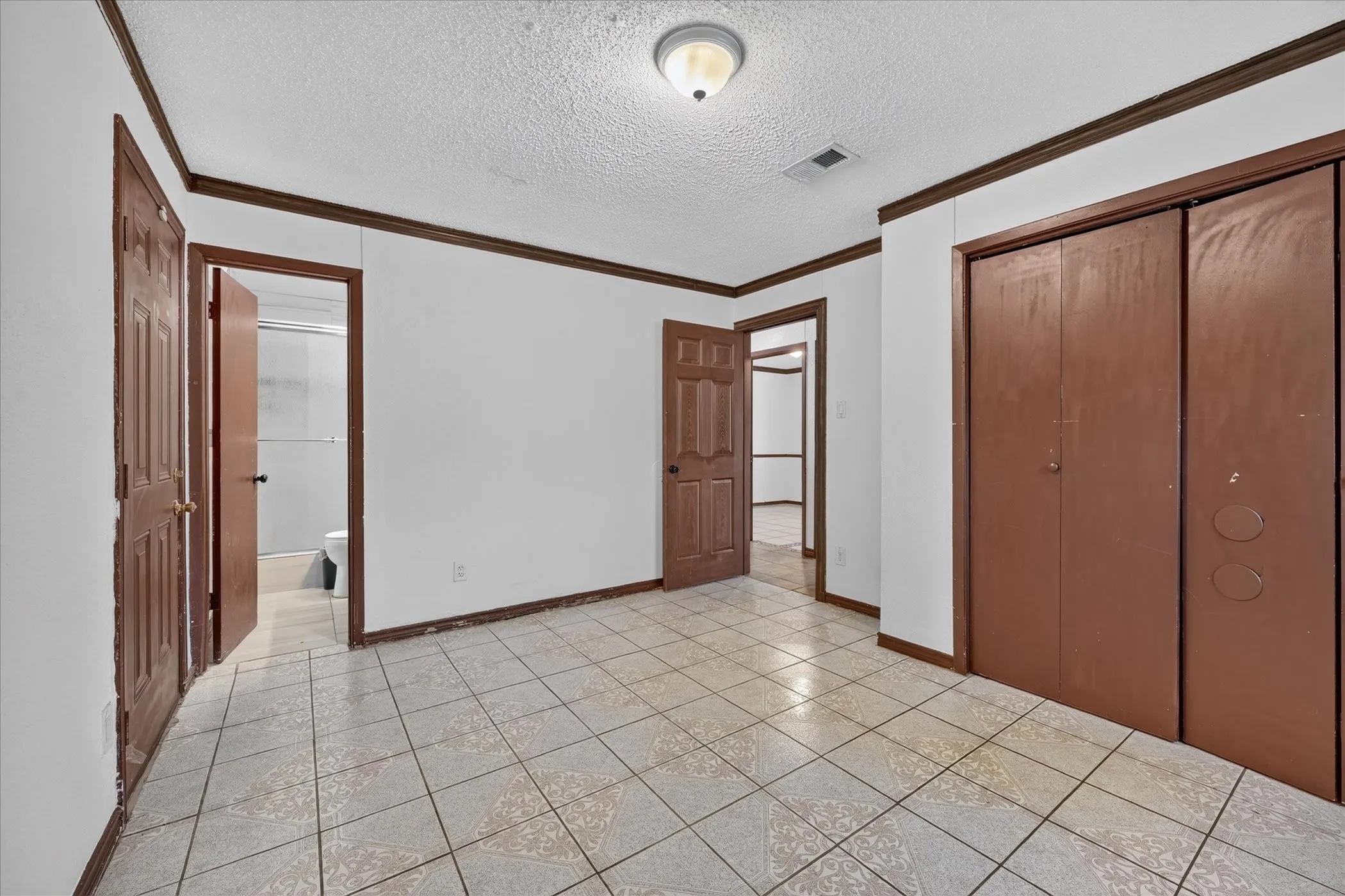 Light-toned tile flooring, white walls, dark wood-finish trim, ceiling-mounted light fixture, and built-in closet with bi-fold doors
