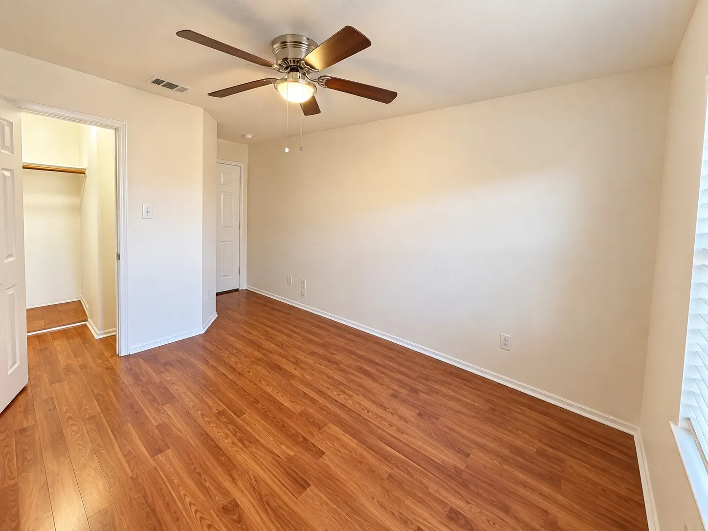 Wood-finish flooring throughout, ceiling fan with integrated lighting, and a closet with shelving