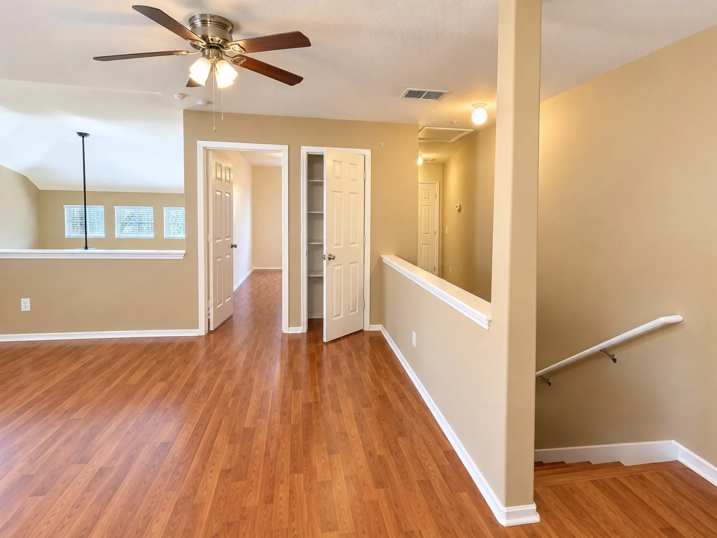 Wood-finish flooring, ceiling fan with light fixture, multiple windows, interior doors, and built-in closet shelving