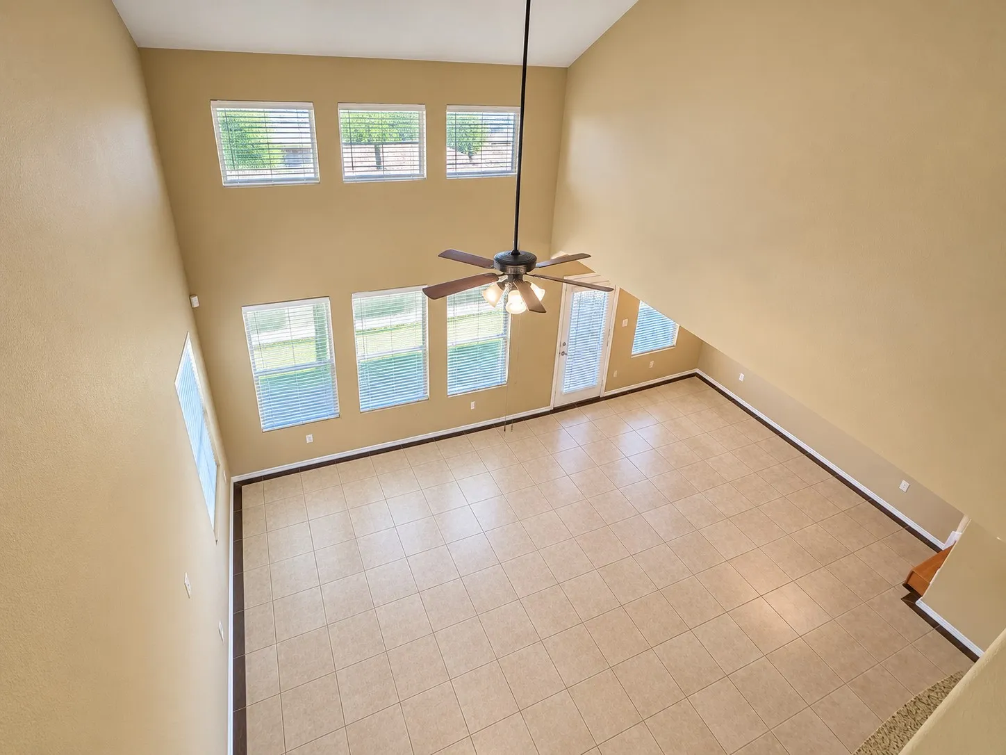 Soaring ceilings with a ceiling fan, multiple windows, a rear door with integrated blinds, and tile flooring