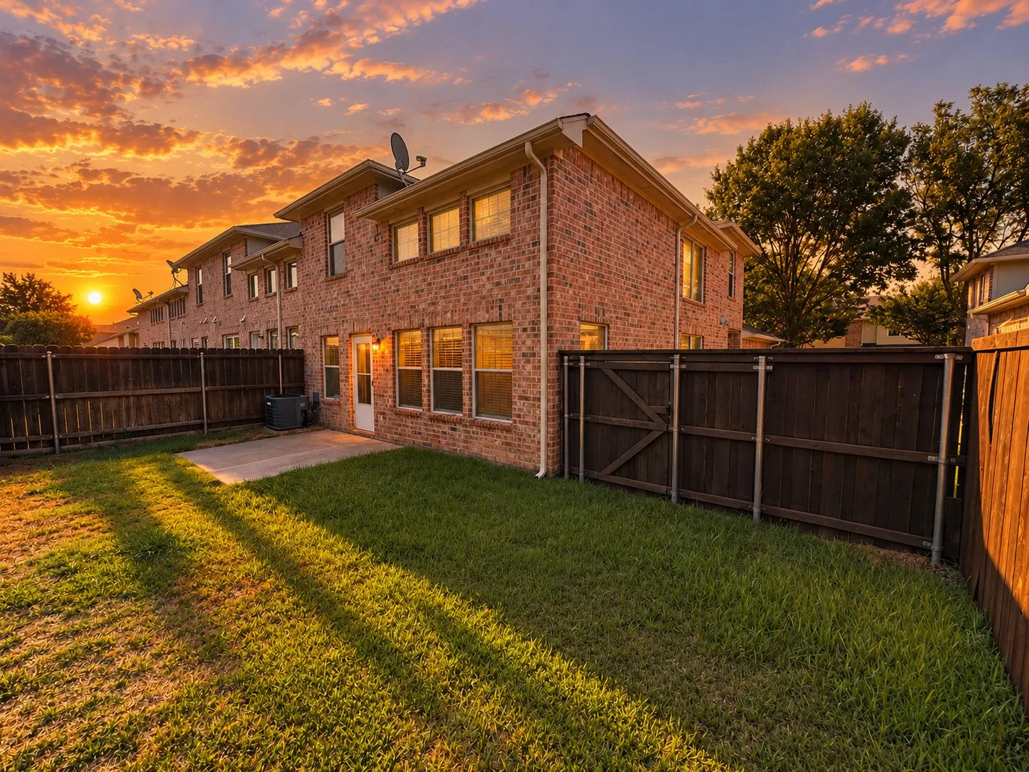 Fenced backyard with a concrete patio, brick exterior, and multiple windows
