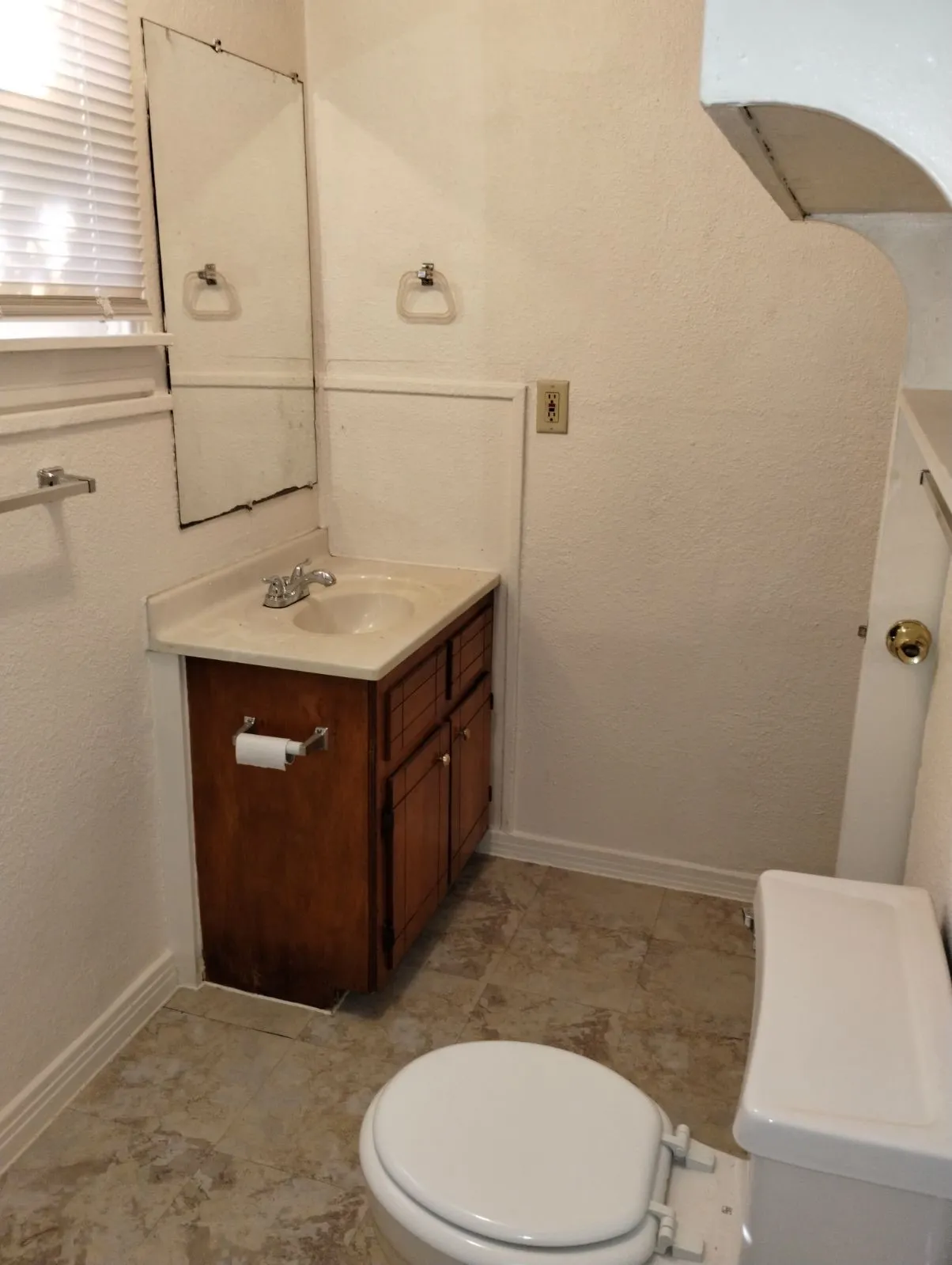 Vanity with integrated sink, wood-finish cabinetry, neutral-toned flooring, and wall-mounted mirror