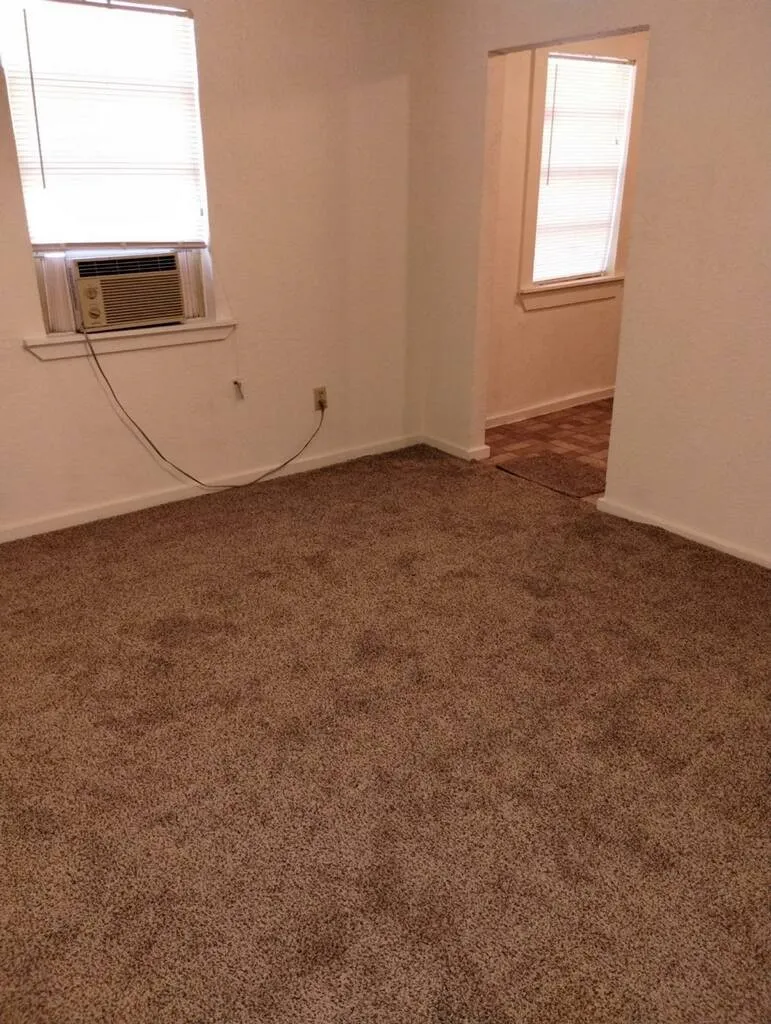 Carpeted flooring, white painted walls, window with blinds, and an entryway