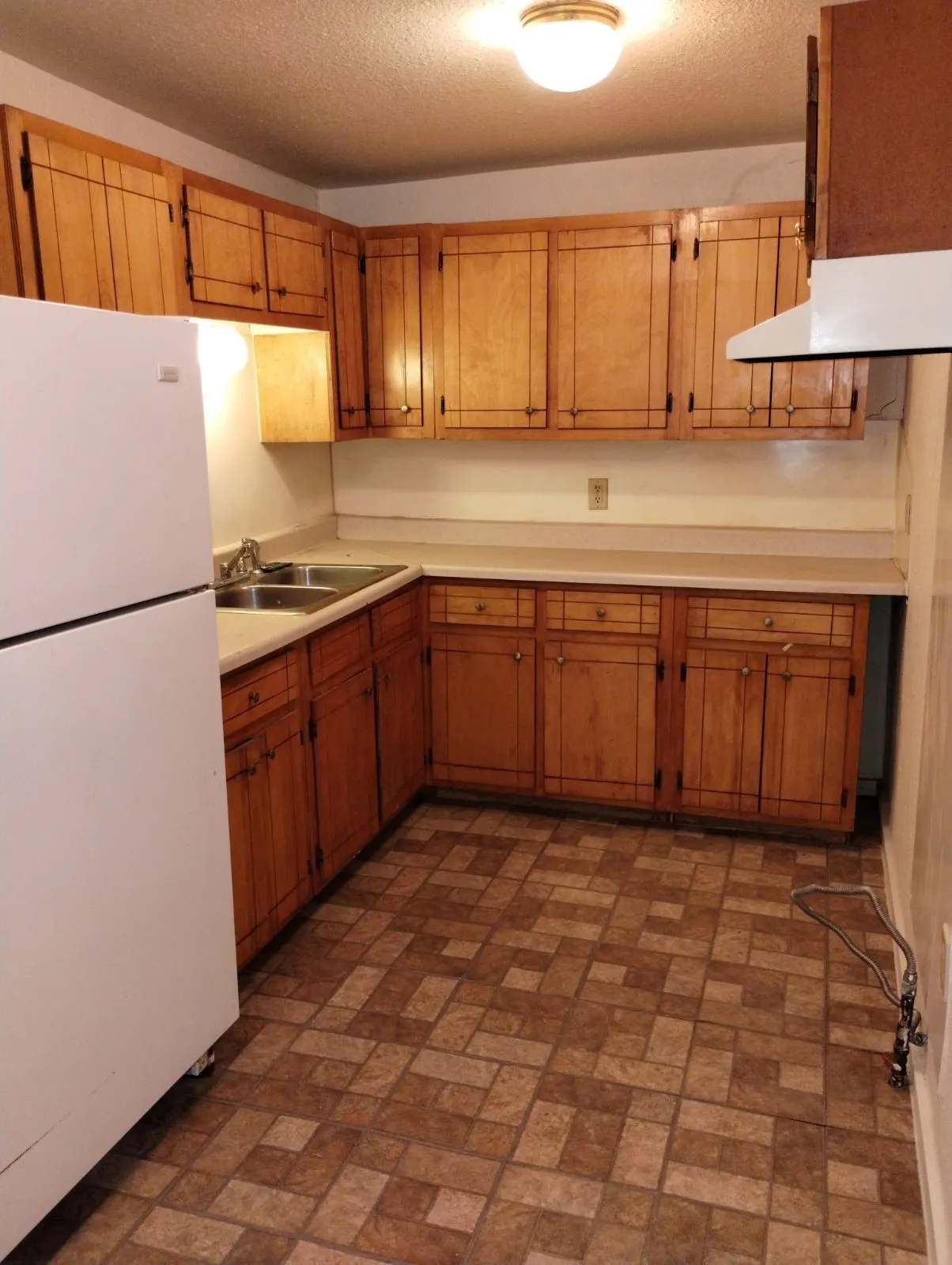 Kitchen featuring wood cabinetry, laminate countertops, a double basin stainless steel sink, and patterned floor tiling
