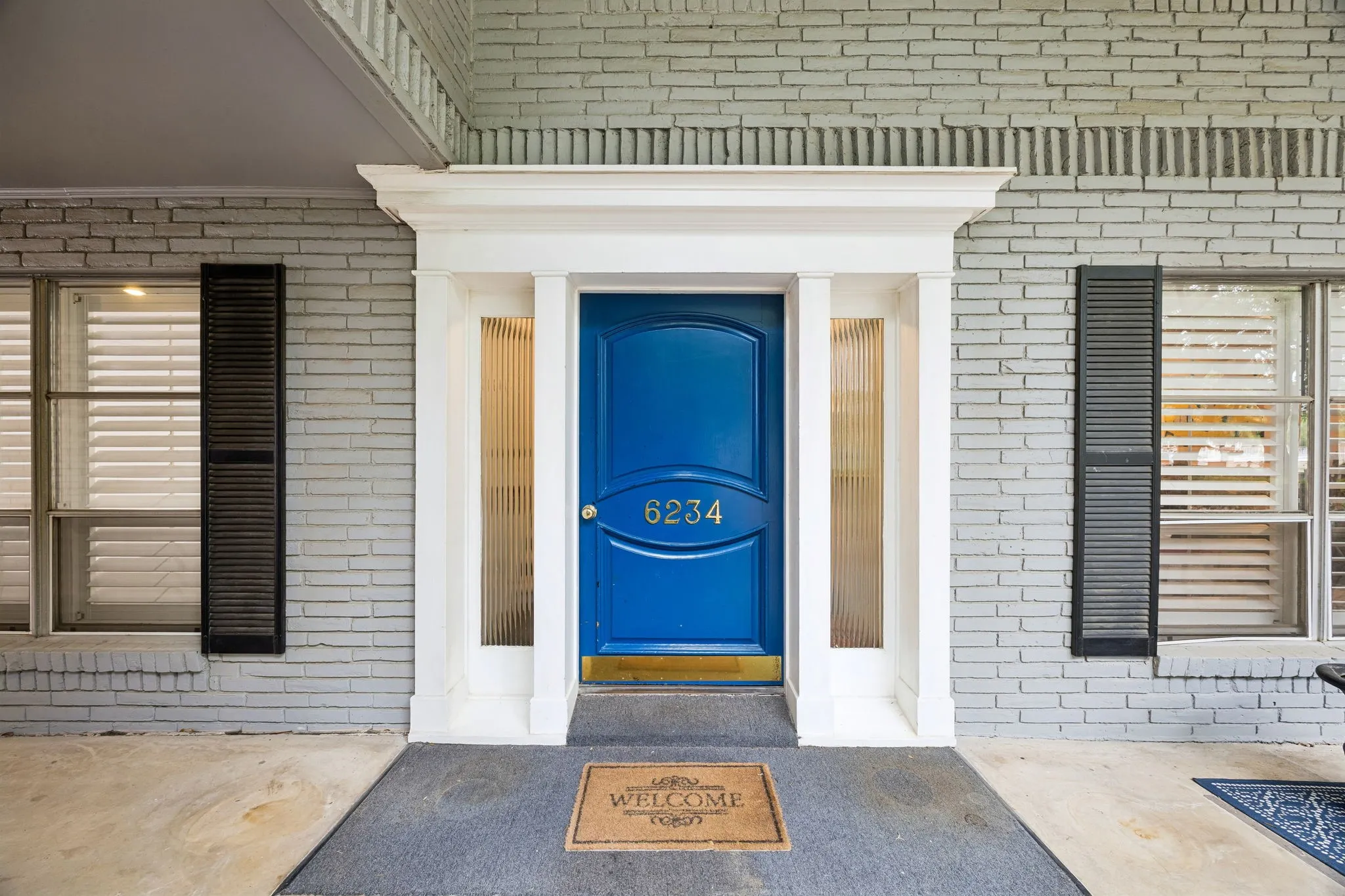 Brick exterior with decorative lintel detailing, prominent blue entry door with transom, white door frame with fluted sidelight windows, and coordinating window shutters